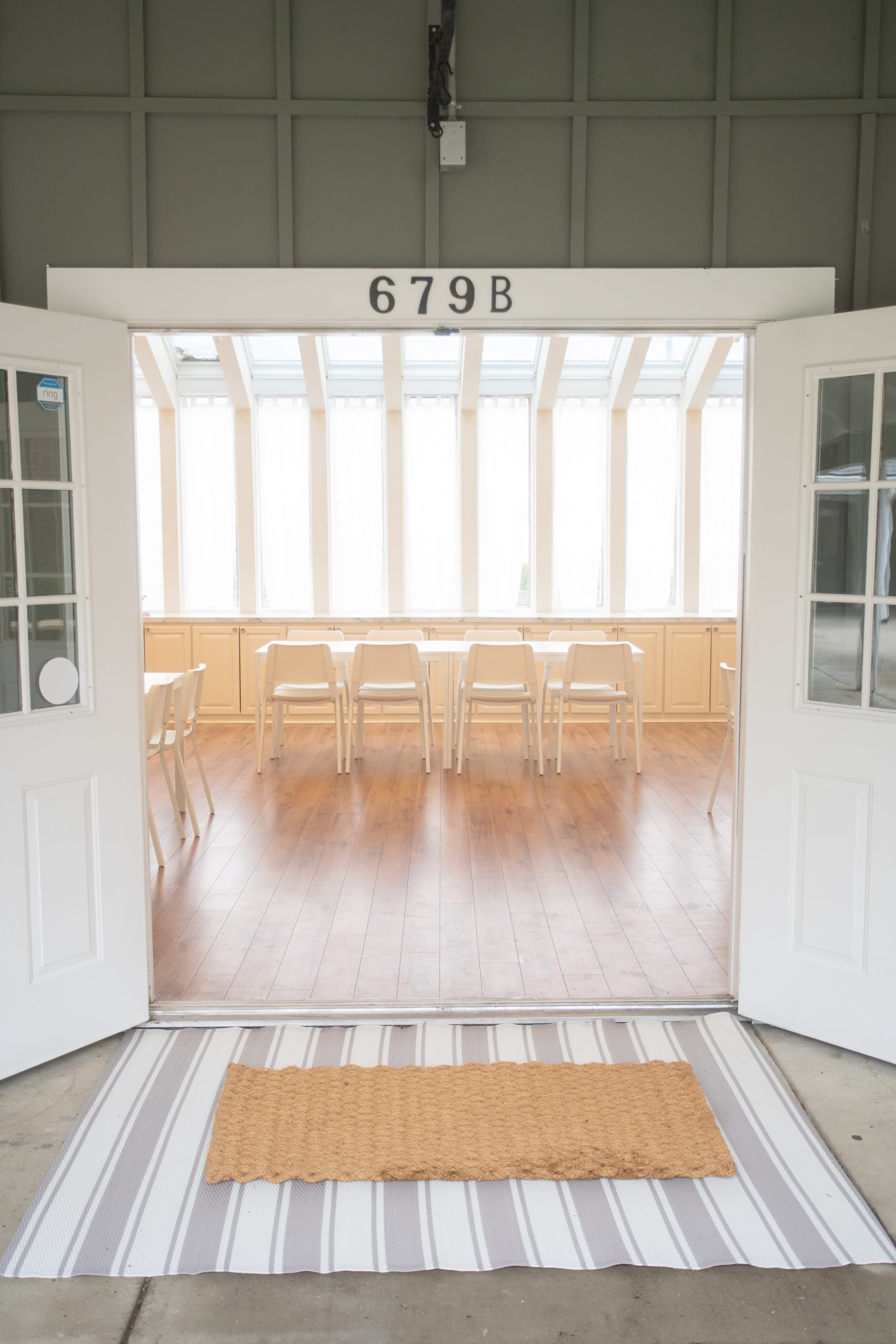 A pair of open double doors leads into a bright room with wooden flooring and several chairs arranged at a long table.