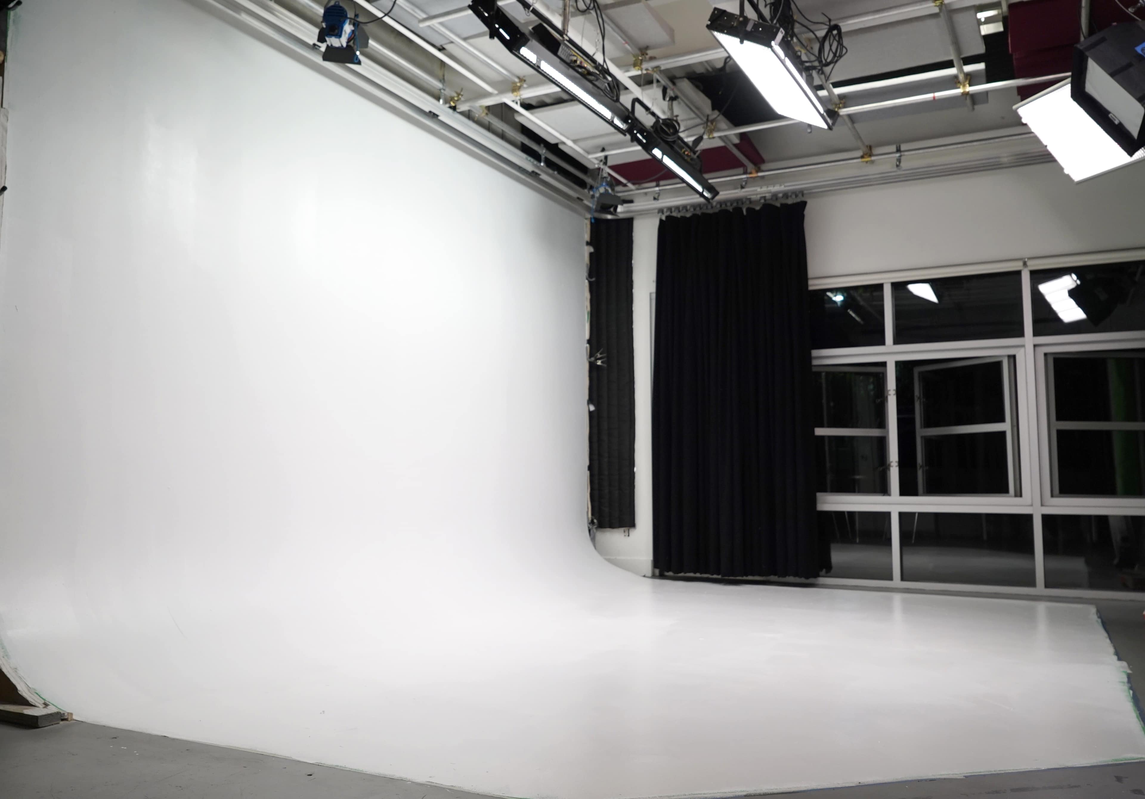 The image shows a well-lit photography studio with a large white backdrop and a dark curtain.