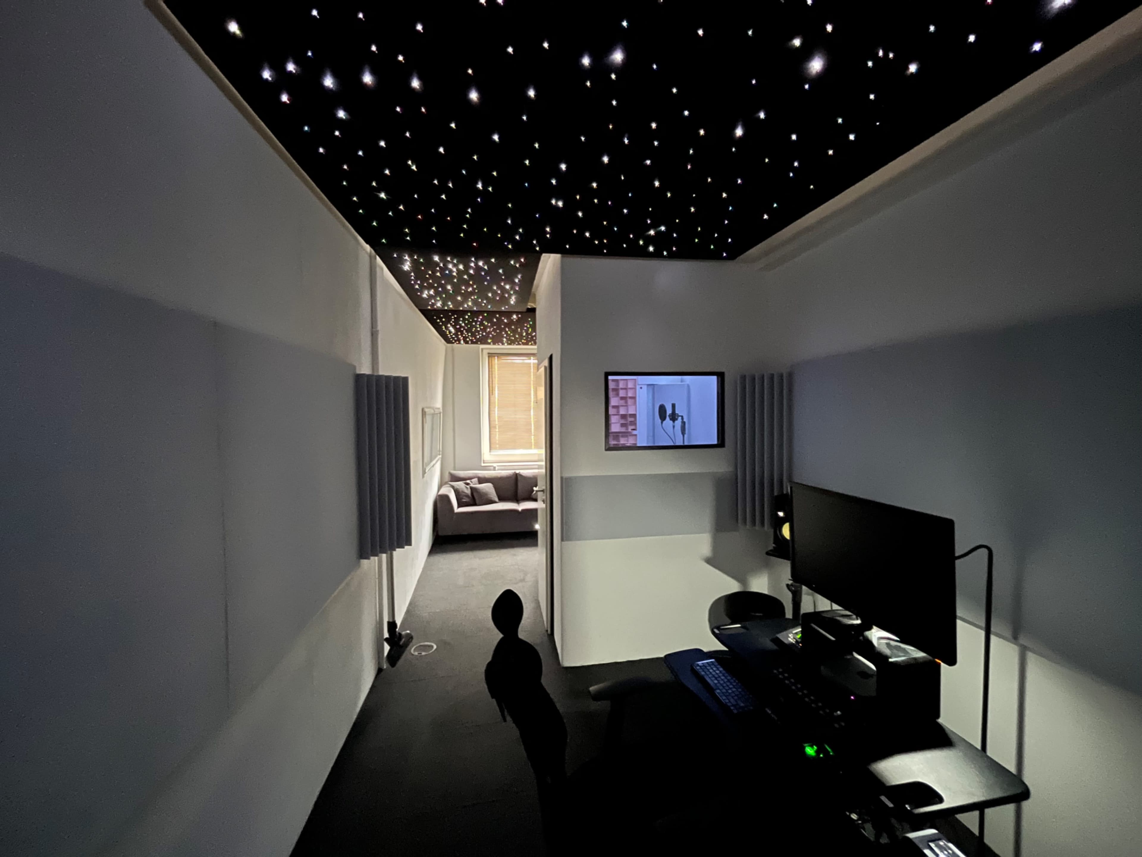A dimly lit corridor leads to a comfortable living area, with a ceiling resembling a starry sky and a workstation on the side.