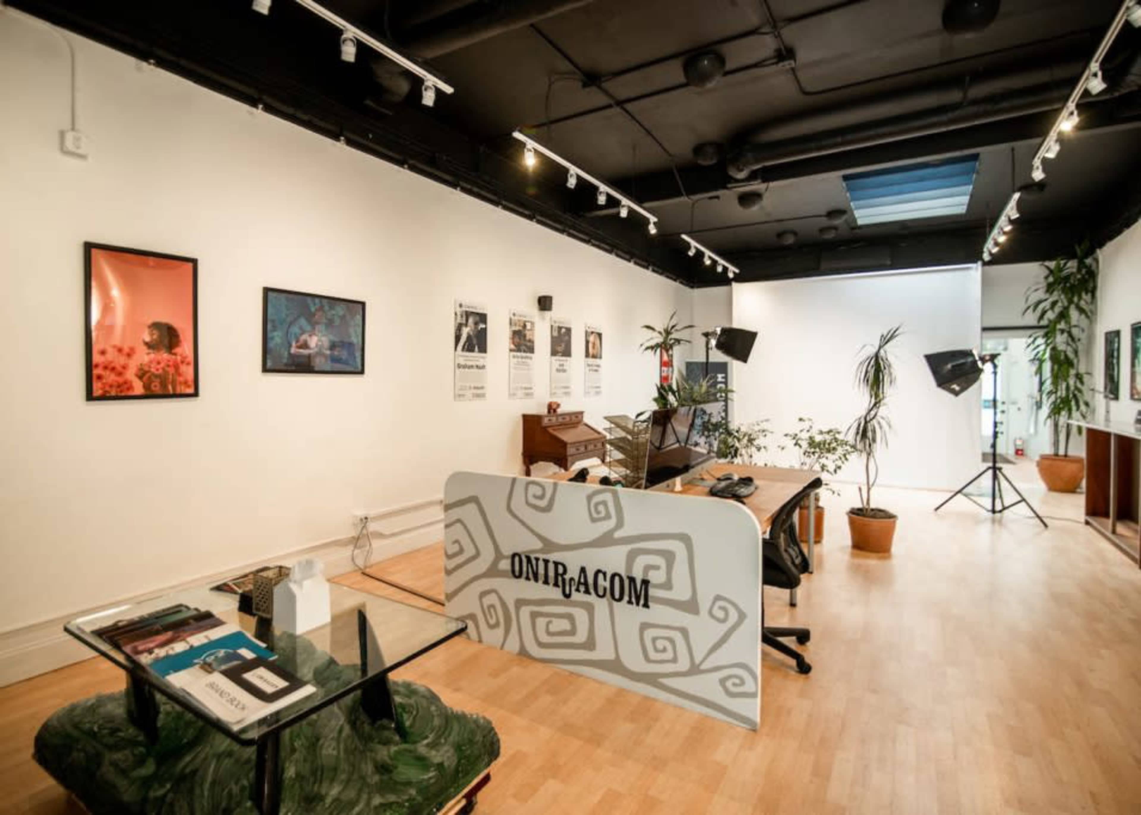 A modern office space with a reception area featuring a desk and office equipment, surrounded by artwork and plants.