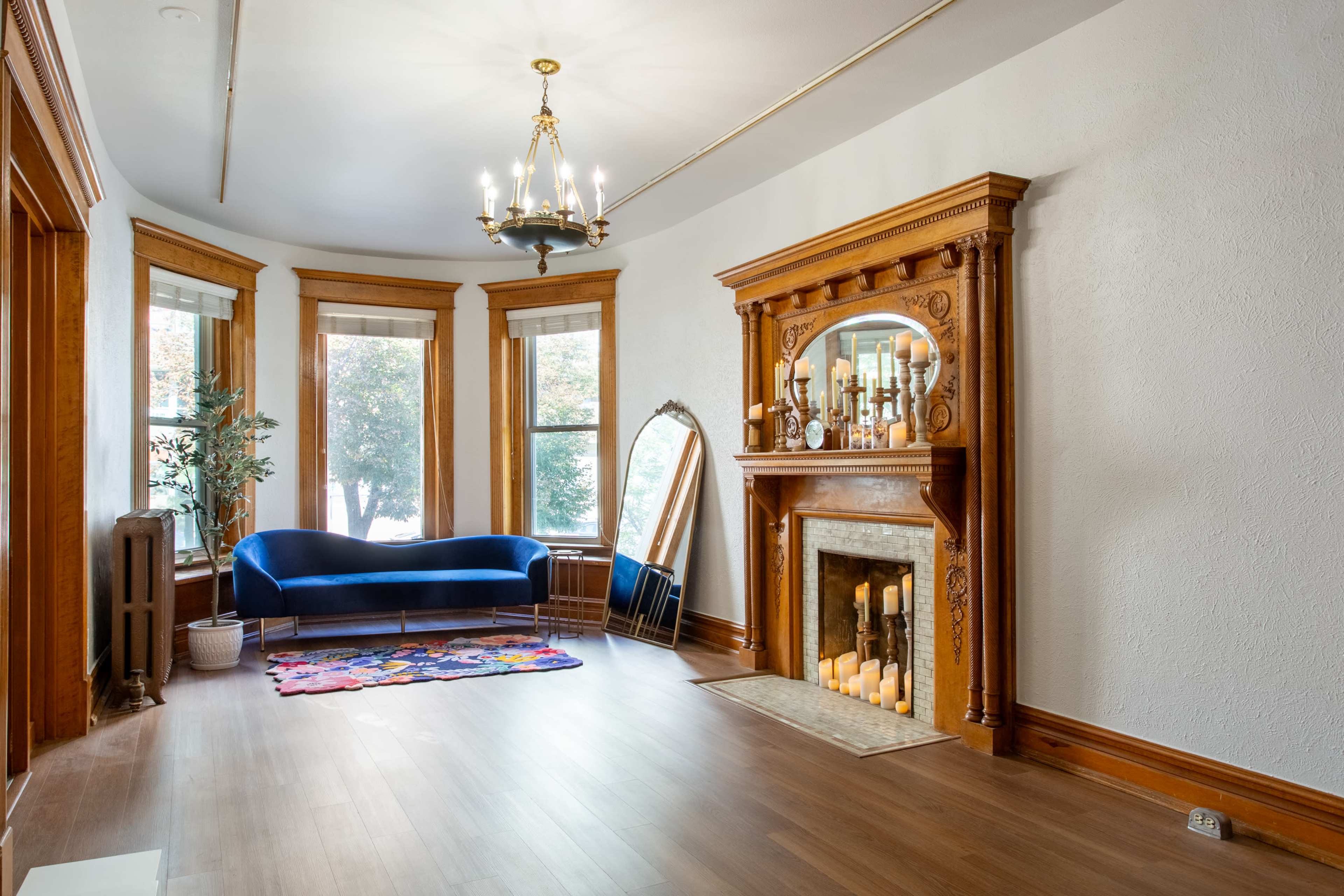 A spacious living room featuring a blue couch, a decorative fireplace with candles, and large windows adorned with curtains.