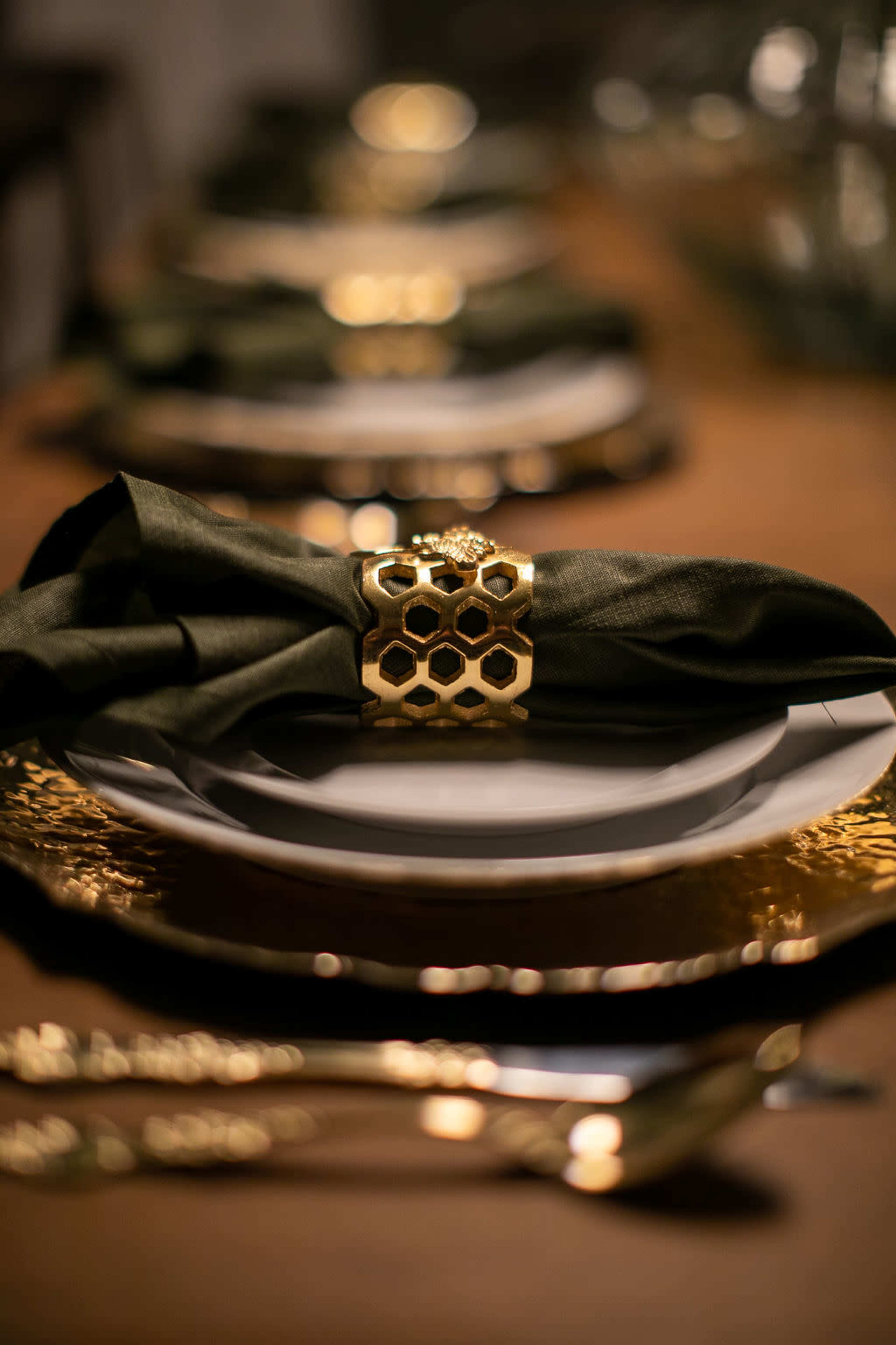 A beautifully set dining table features elegant plates, gold accents, and dark green napkins secured with decorative holders.