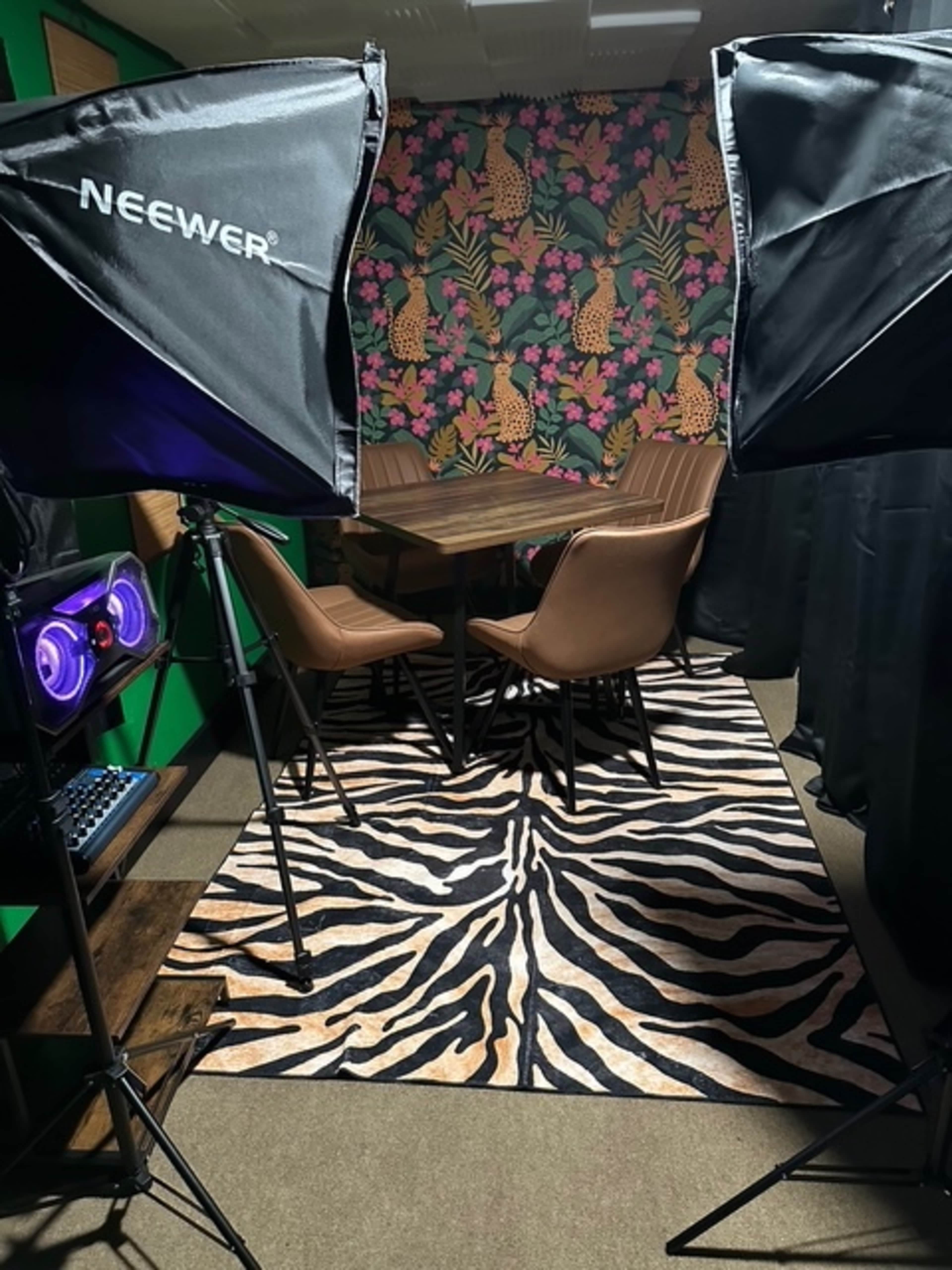 The image shows a well-lit meeting room with a patterned floral wall, a wooden table surrounded by brown chairs, and a tiger-striped rug on the floor.