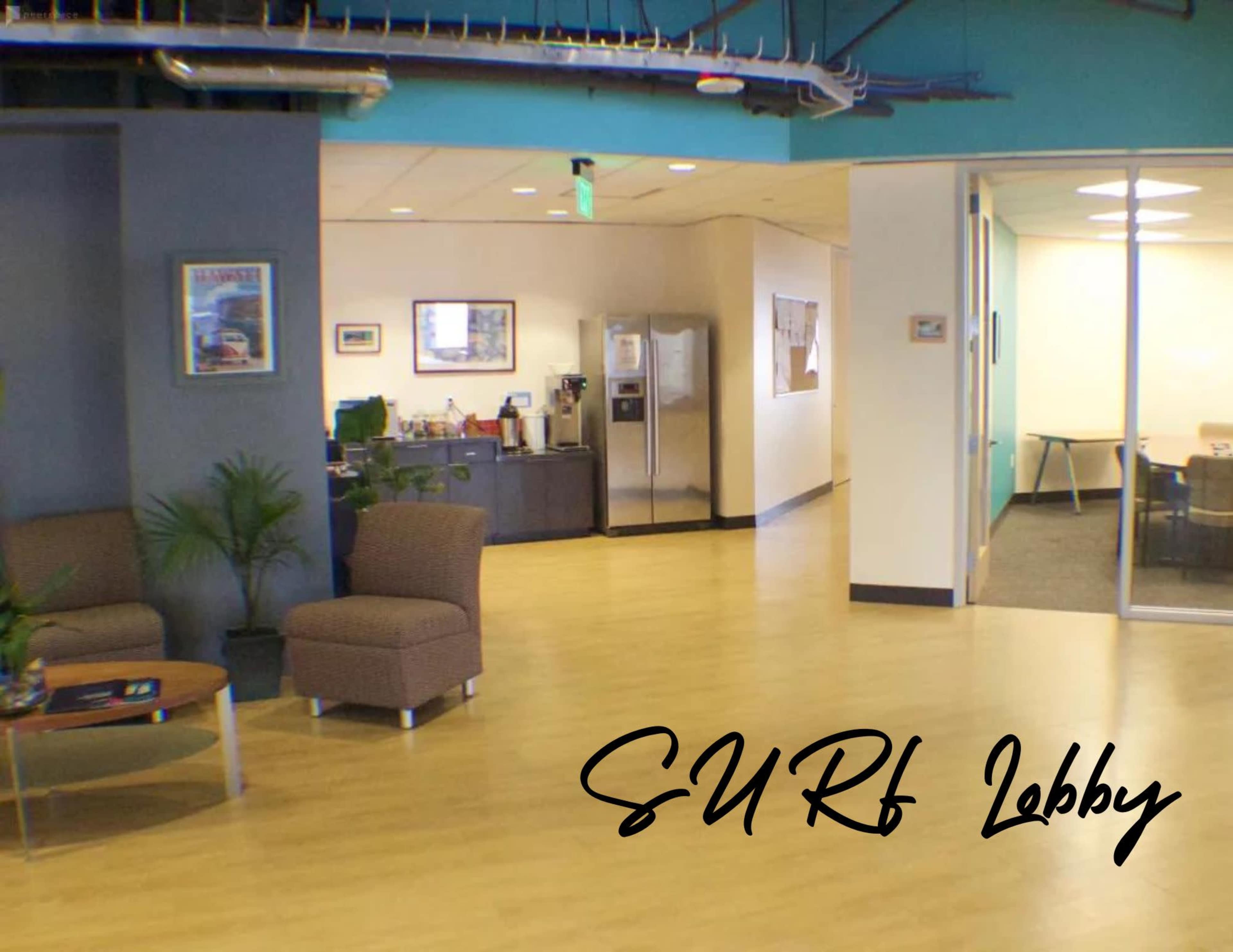 The image shows a modern office lobby area with two chairs, a small table, and a kitchenette in the background.