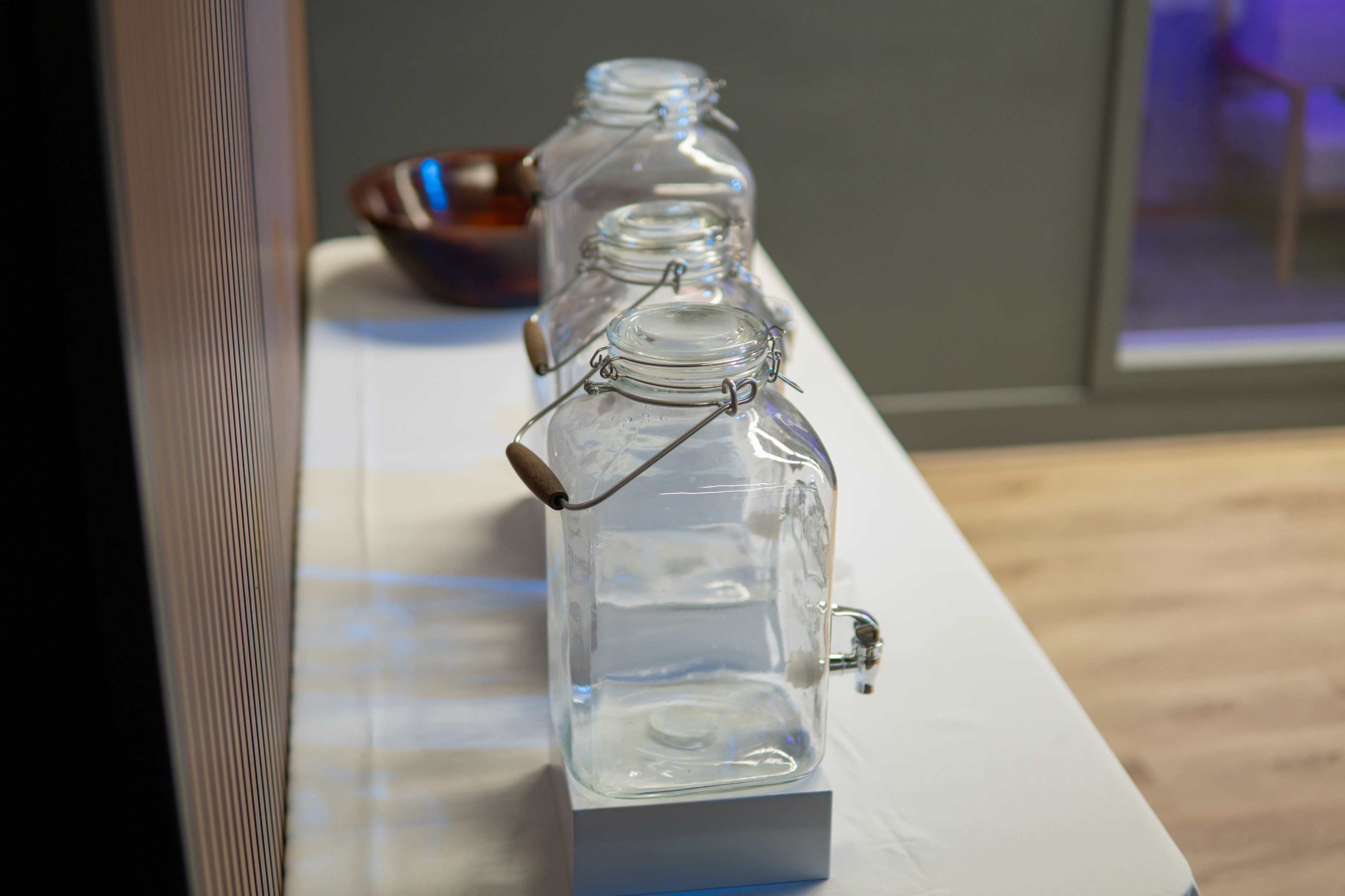 Three empty glass jars with metal lids are placed on a white tablecloth, with a wooden bowl visible in the background.