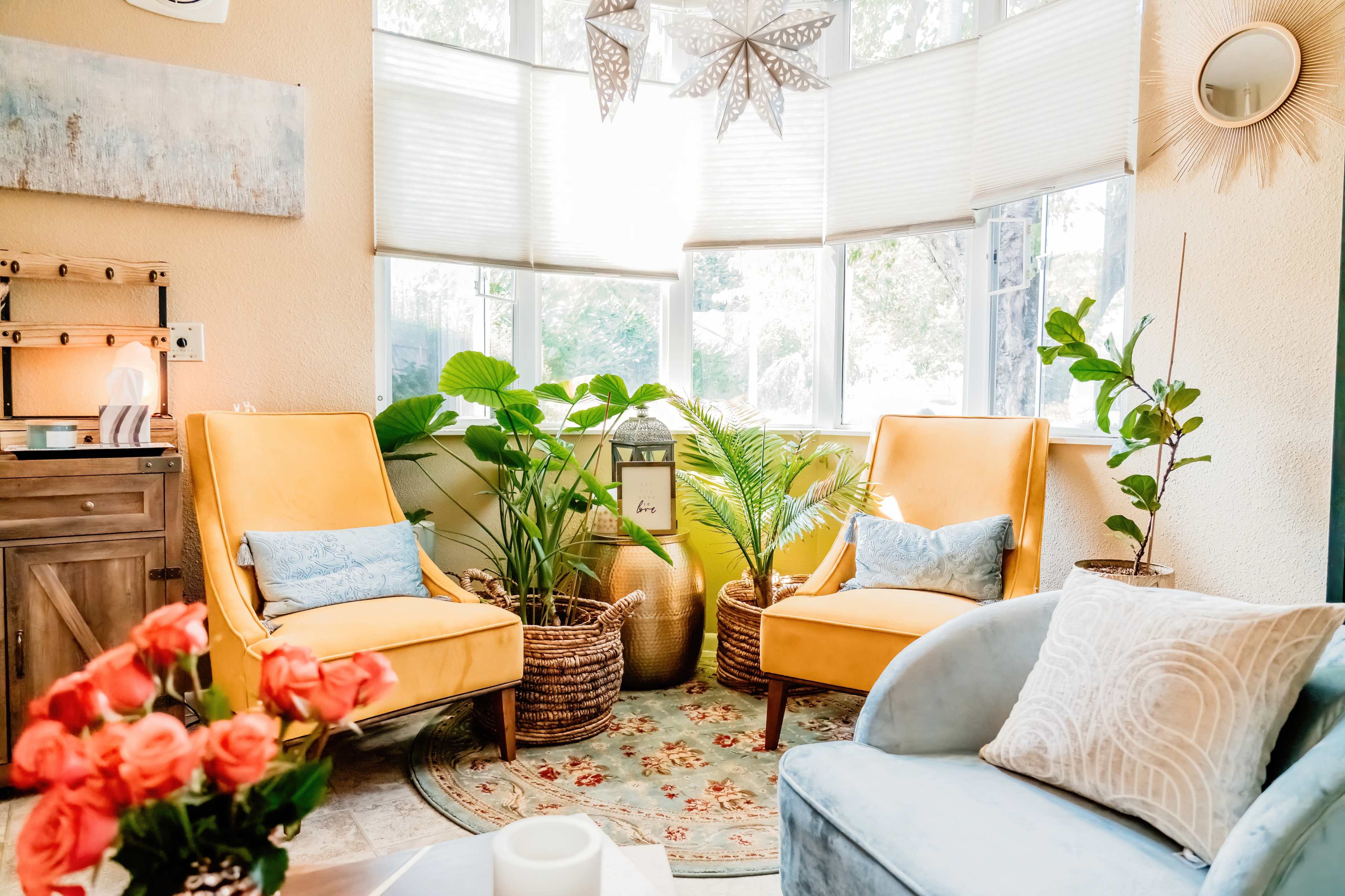 A cozy seating area with two yellow armchairs, a blue couch, and various indoor plants surrounded by natural light.