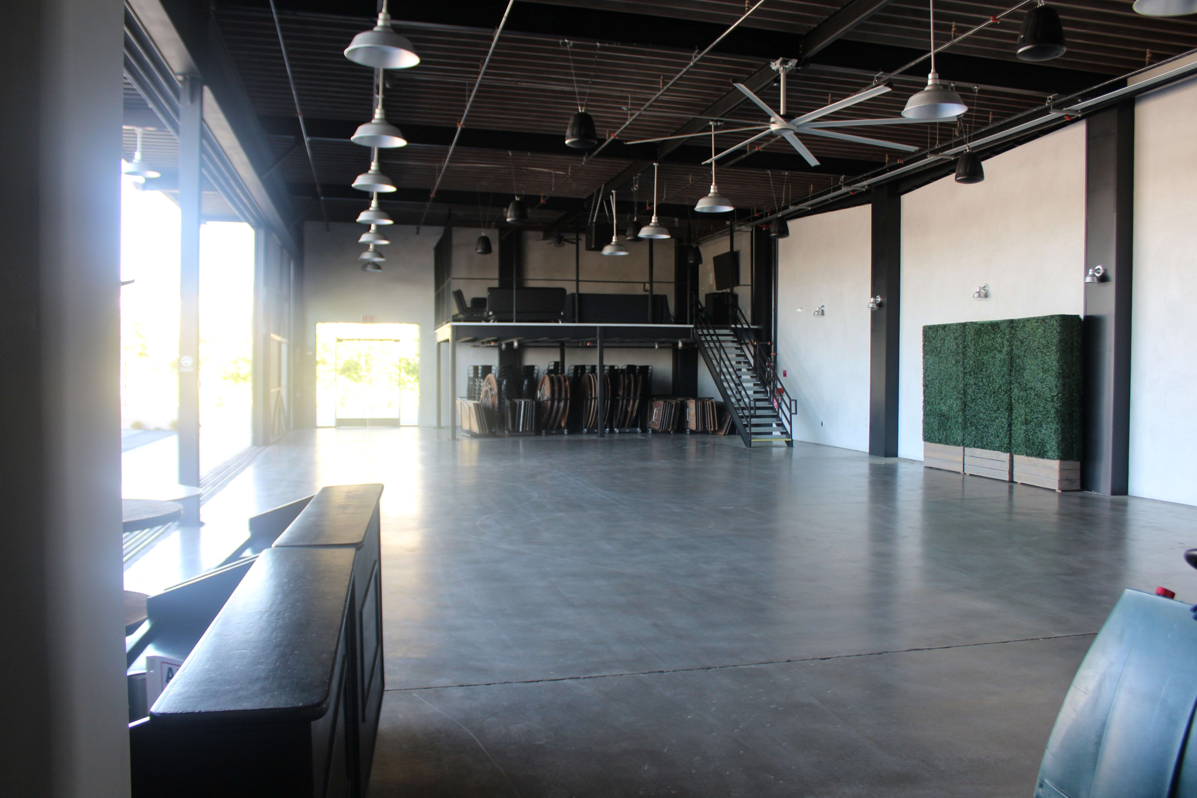 A spacious, empty industrial interior with a concrete floor, large windows, and a staircase in the back.