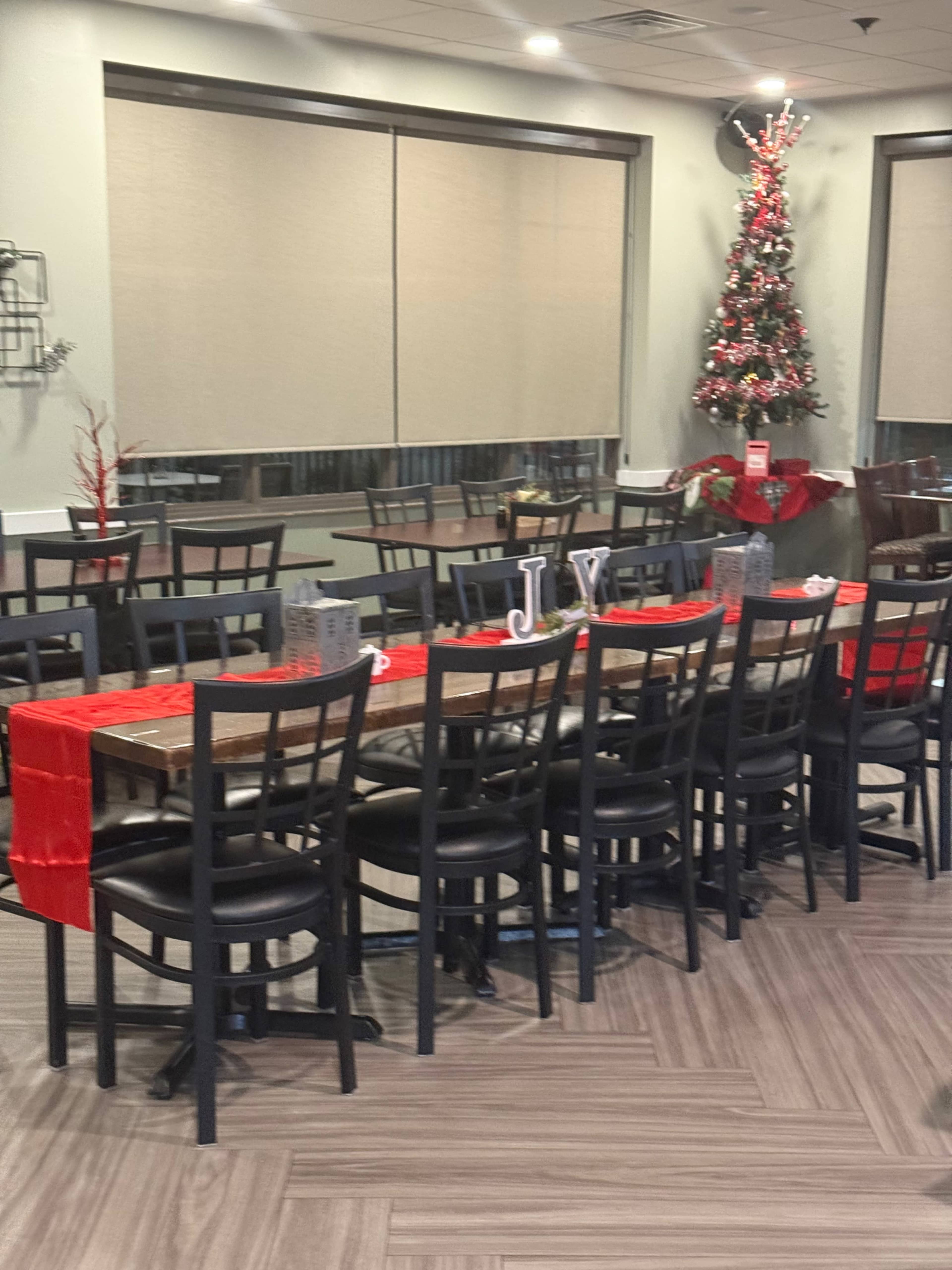 The image shows a restaurant dining area with black chairs, wooden tables, and a decorated Christmas tree in the corner.