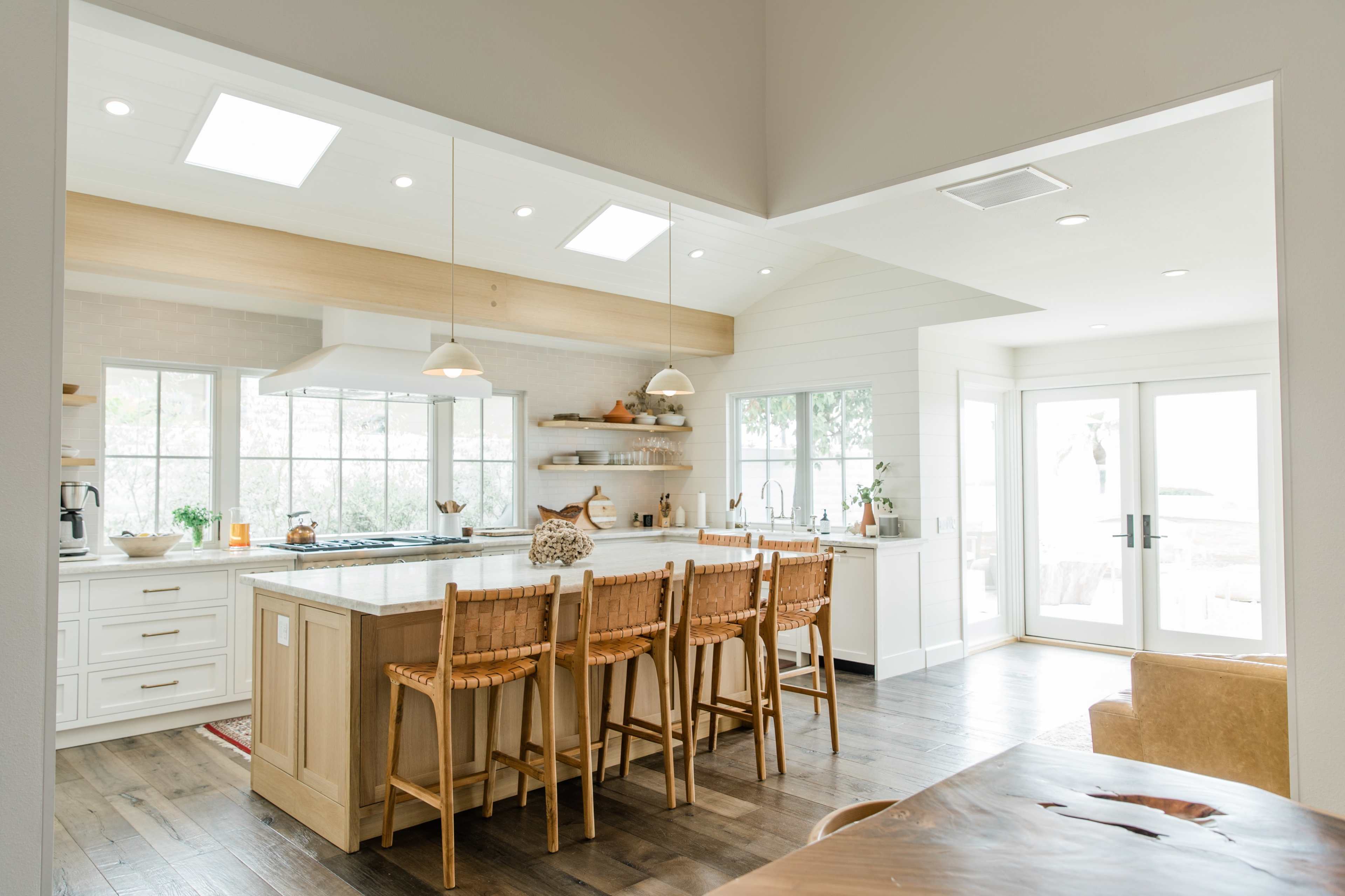 A modern kitchen features an island with seating, large windows, and white cabinets.