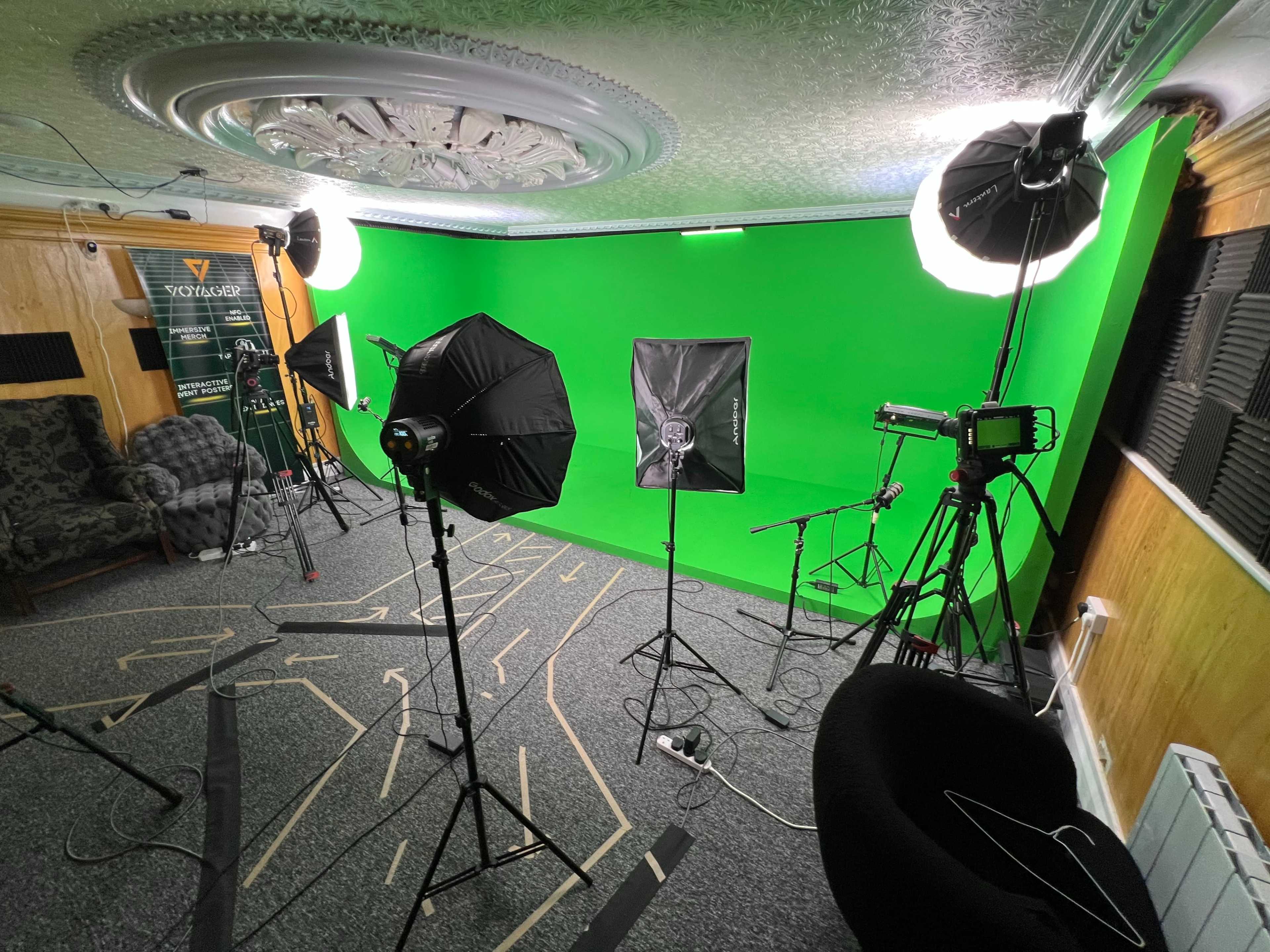 The image shows a room equipped with lighting equipment and a green backdrop, typically used for filming or photography.