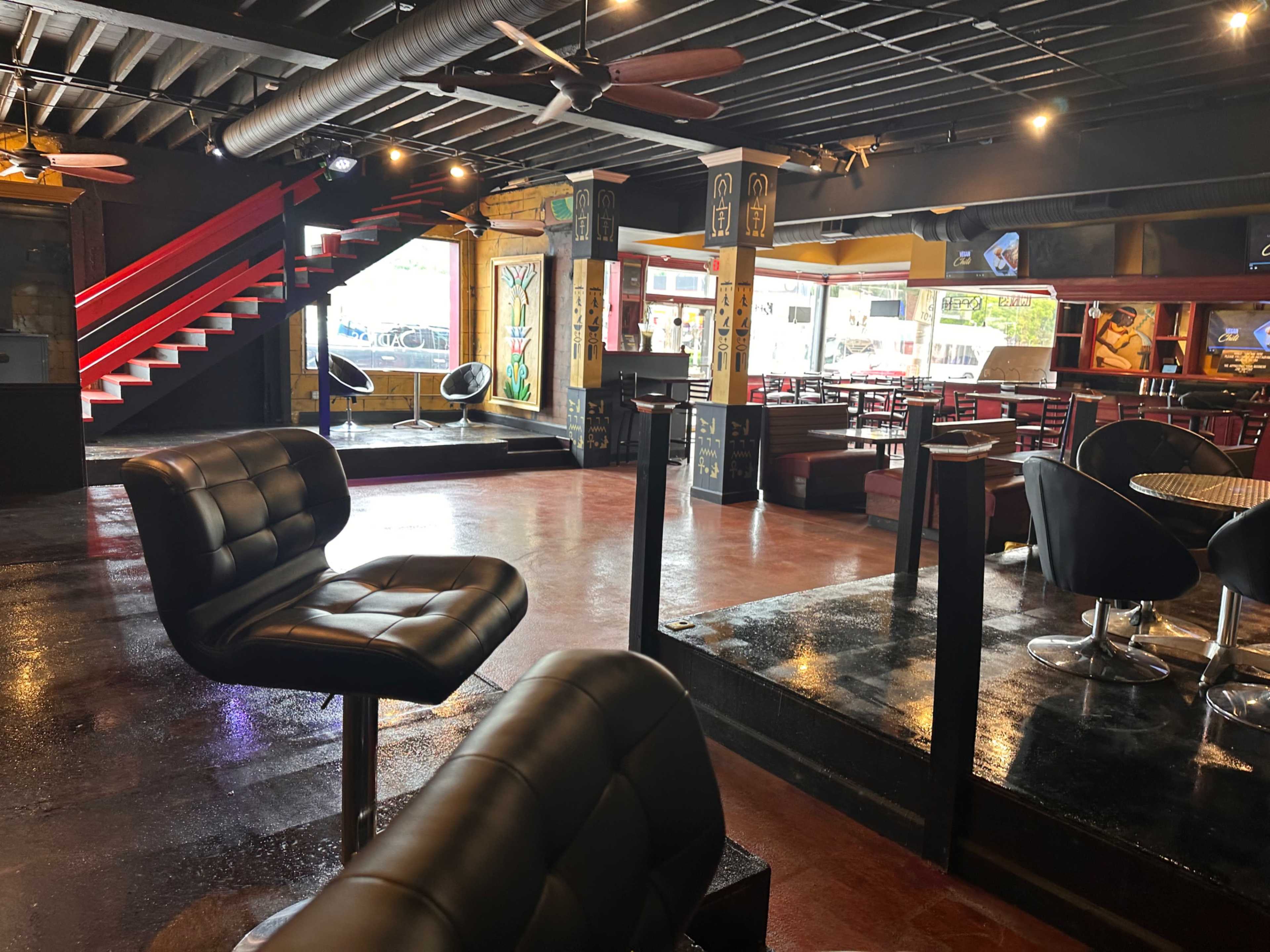 An empty bar or lounge area with modern furniture, dark seating, and a staircase leading to a higher level.