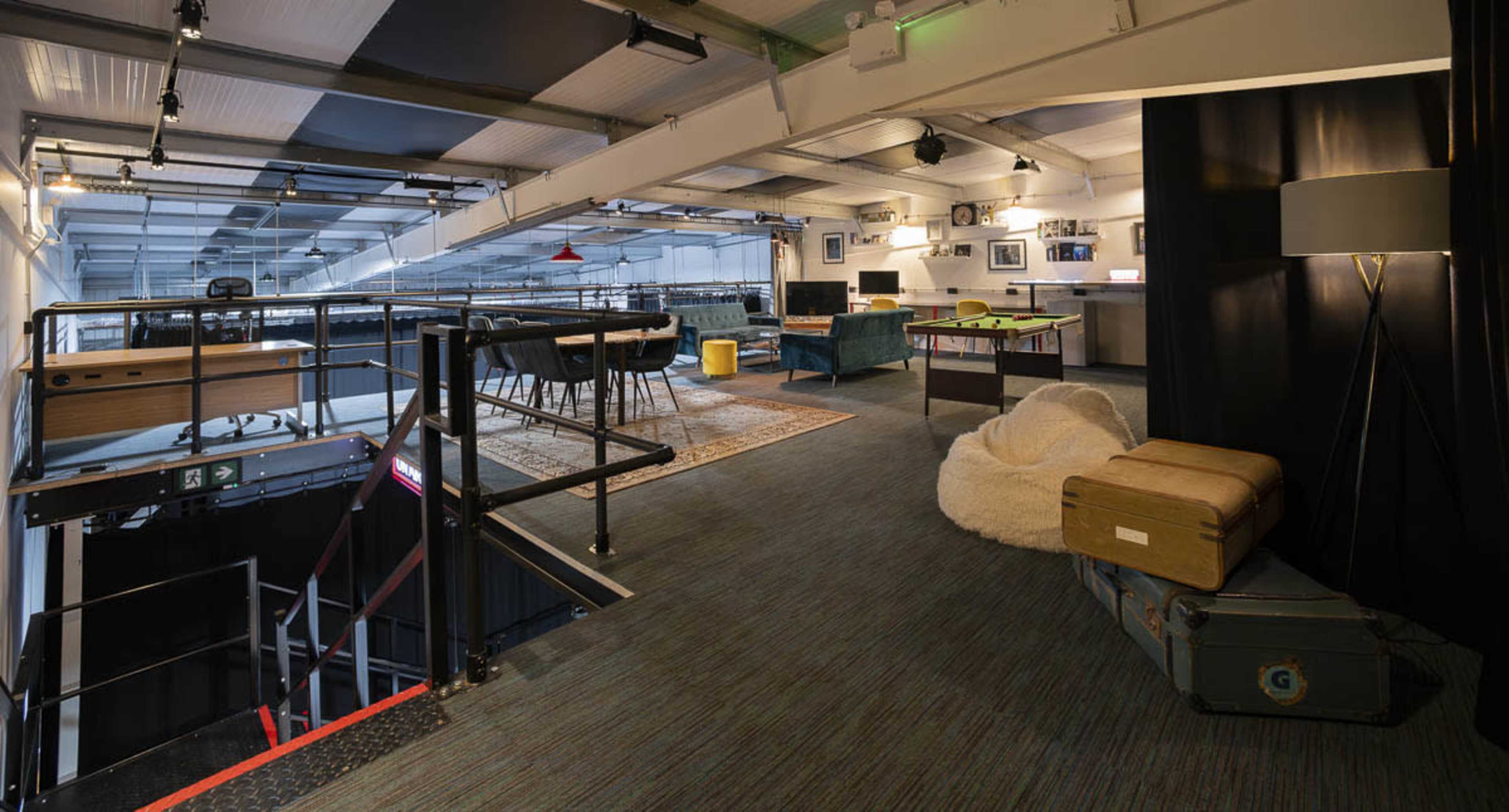 A spacious, modern loft-style office area with a game table, lounge seating, and a dining space.