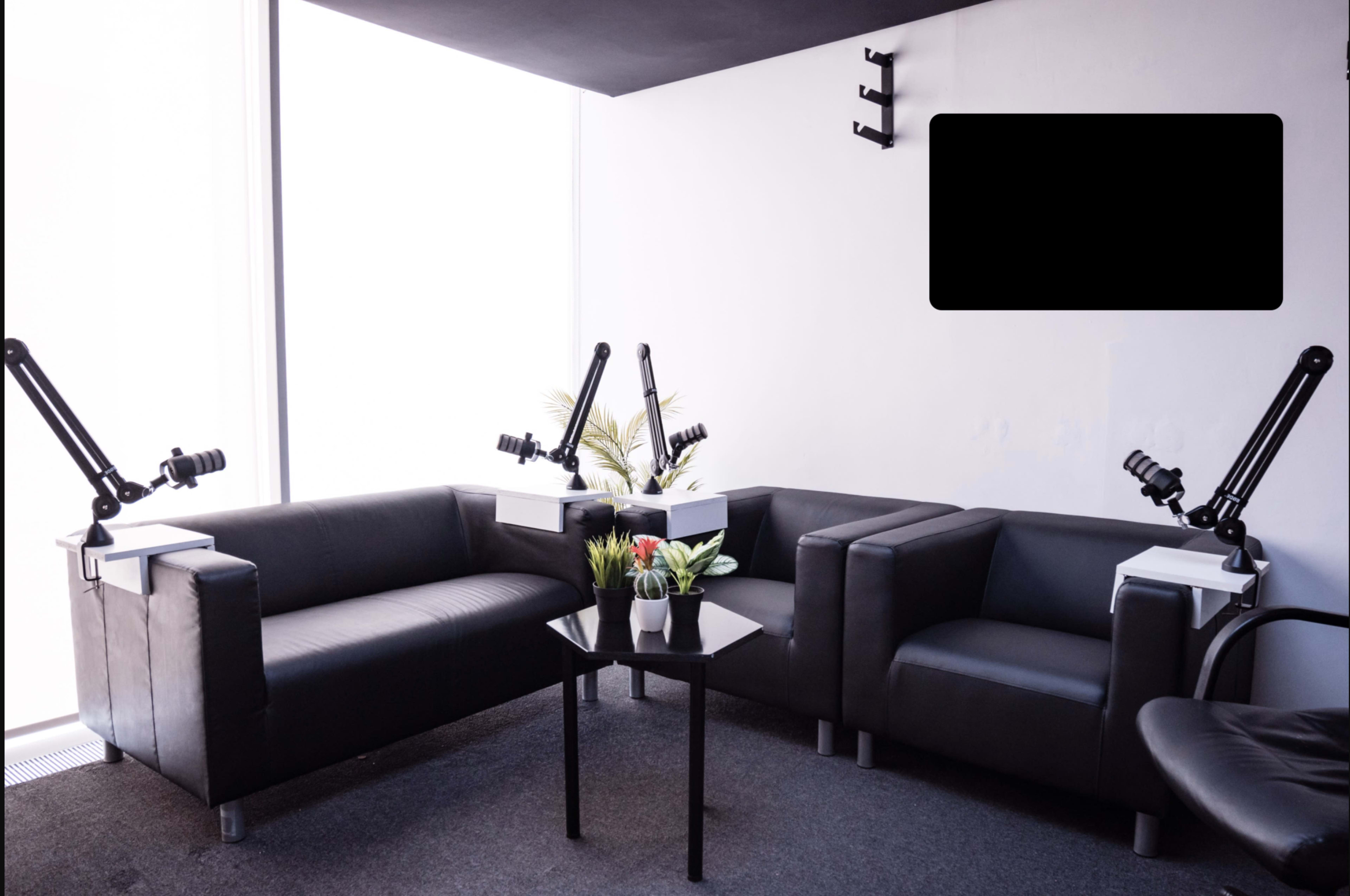 A minimalist seating area with two black sofas, a small black table, and adjustable arm lamps, situated in a well-lit room with large windows.