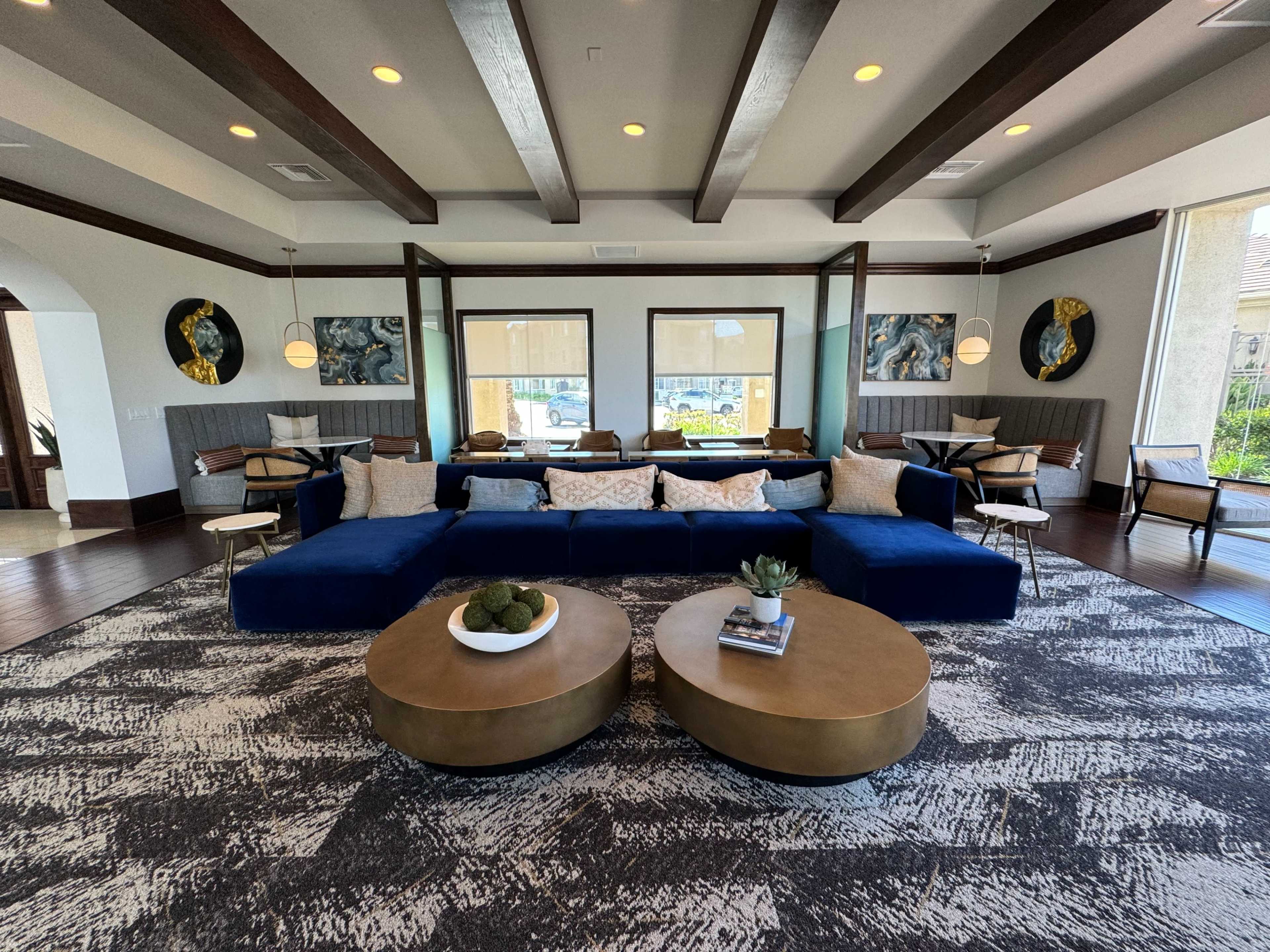 A modern lounge area with navy blue sectional sofas, round coffee tables, and large windows framed by decorative artwork and comfortable seating.