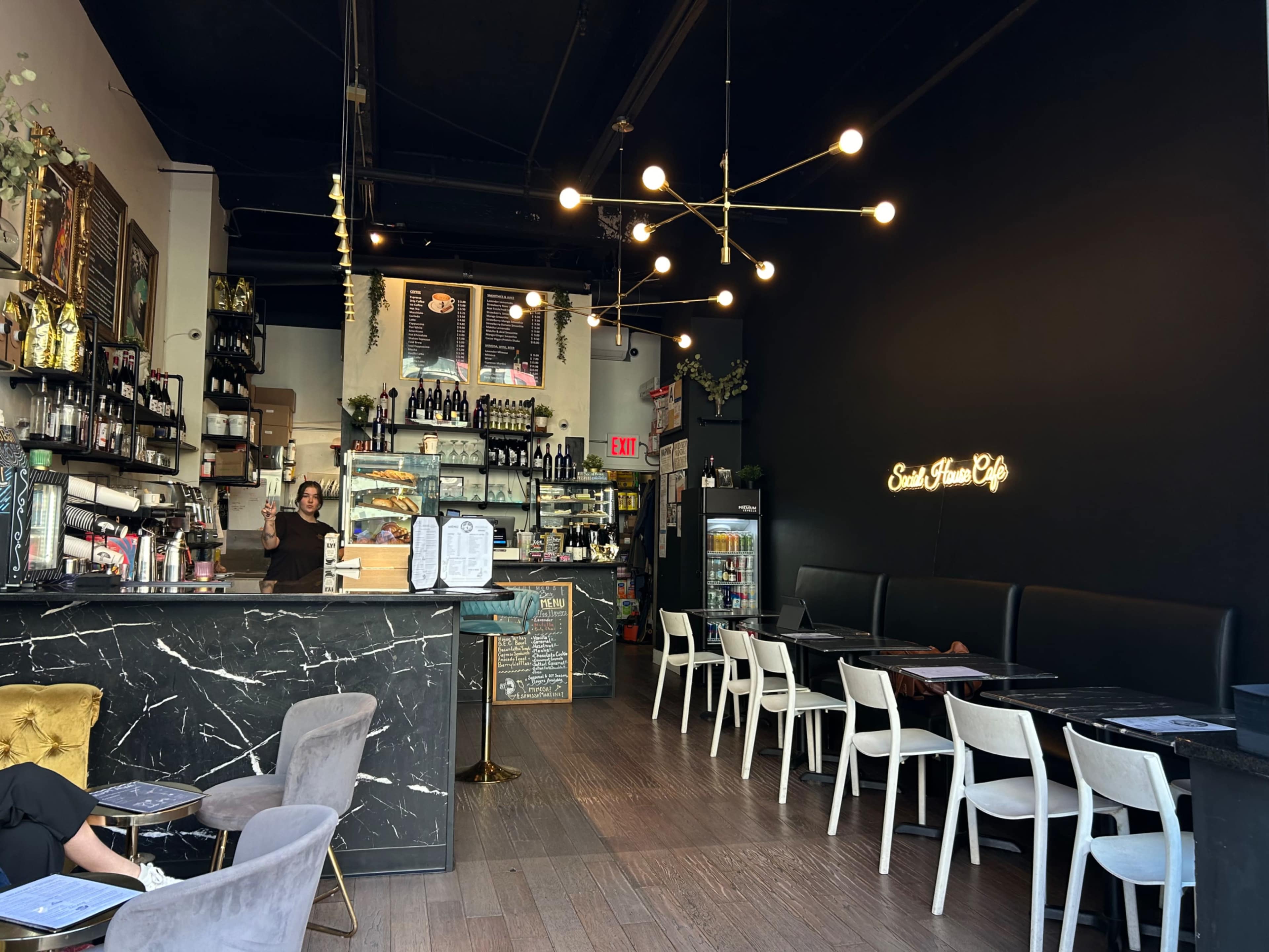 The image shows a modern café interior with a marble counter, a variety of shelves filled with products, and seating arrangements including white chairs and tables.