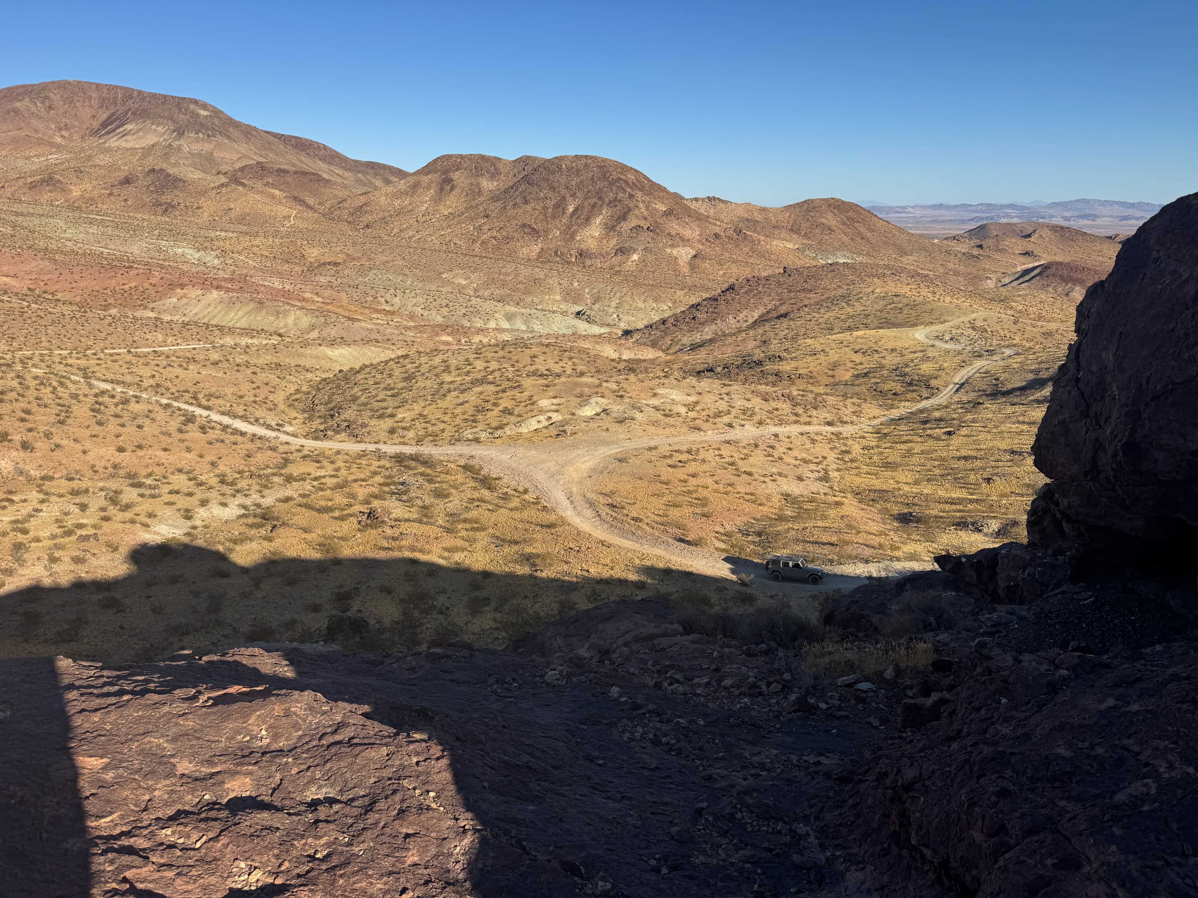 The image depicts a rugged, arid landscape with hills and a winding dirt road leading through the terrain.