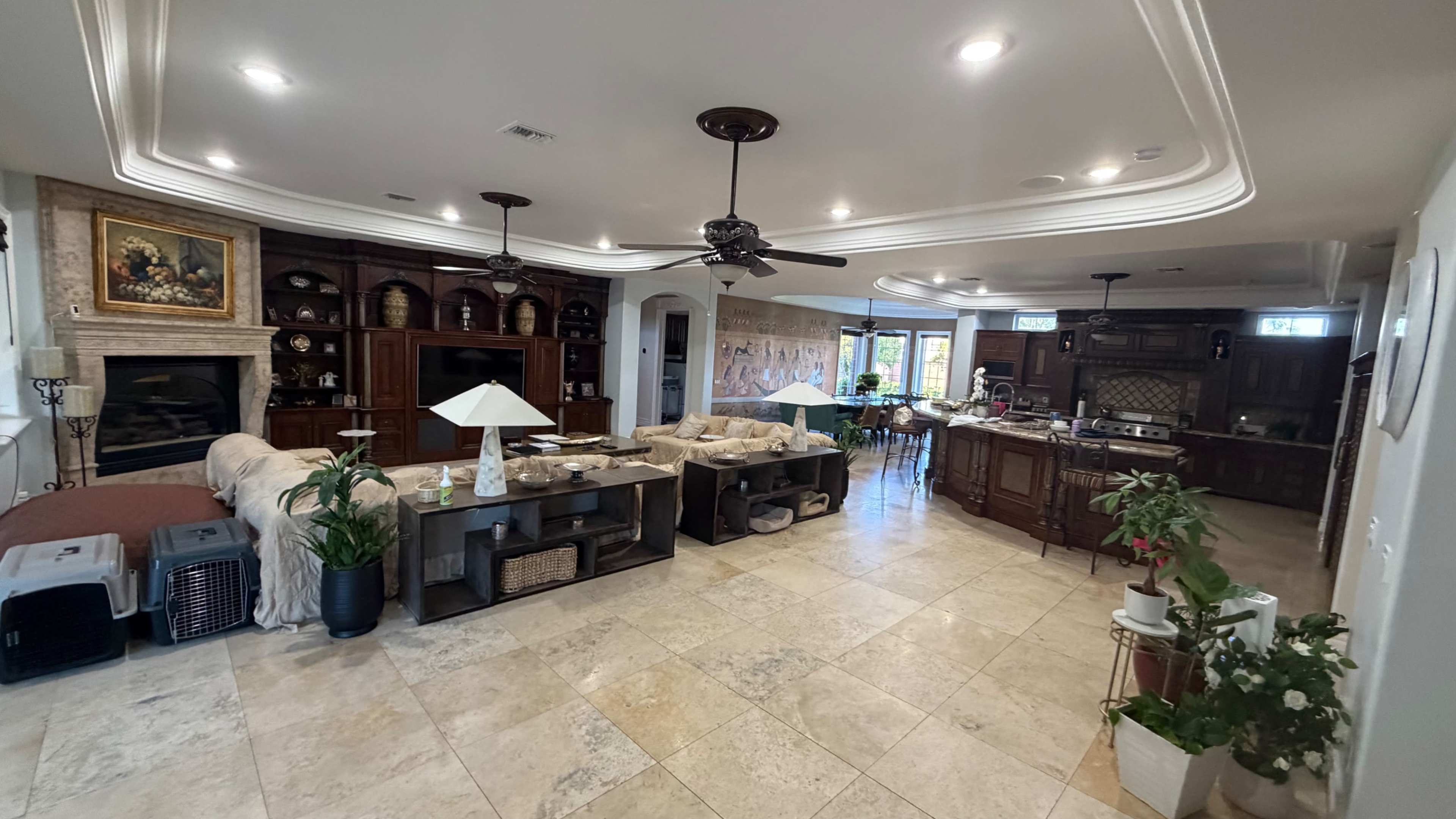 The image shows a spacious living area with a combination of a seating arrangement, a dining space, and an open kitchen, all featuring tiled flooring and wooden furnishings.