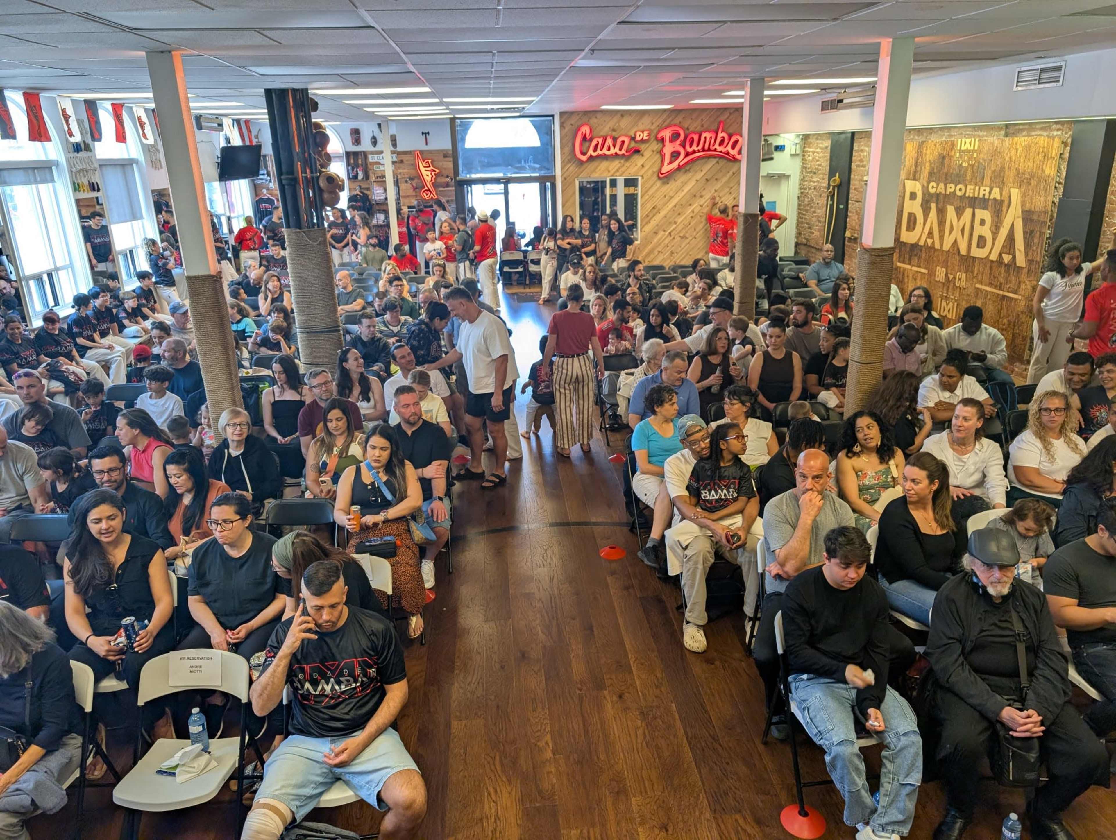 A large crowd gathers inside a venue with rows of chairs, decorated with flags and wooden accents, as people wait for an event to begin.