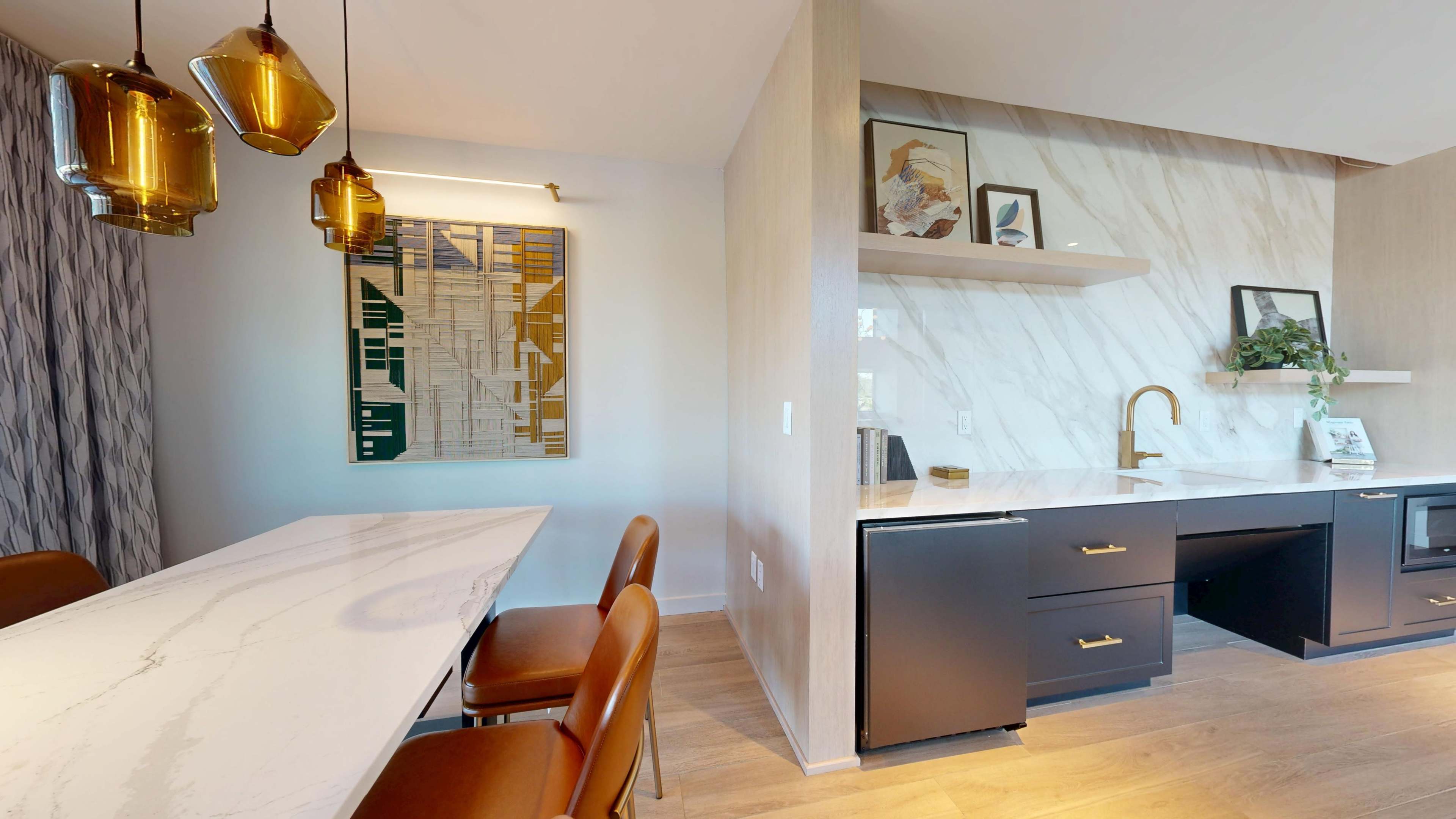 The image shows a modern kitchen area featuring a marble backsplash, black cabinetry, a dining table with brown leather chairs, and decorative wall art.