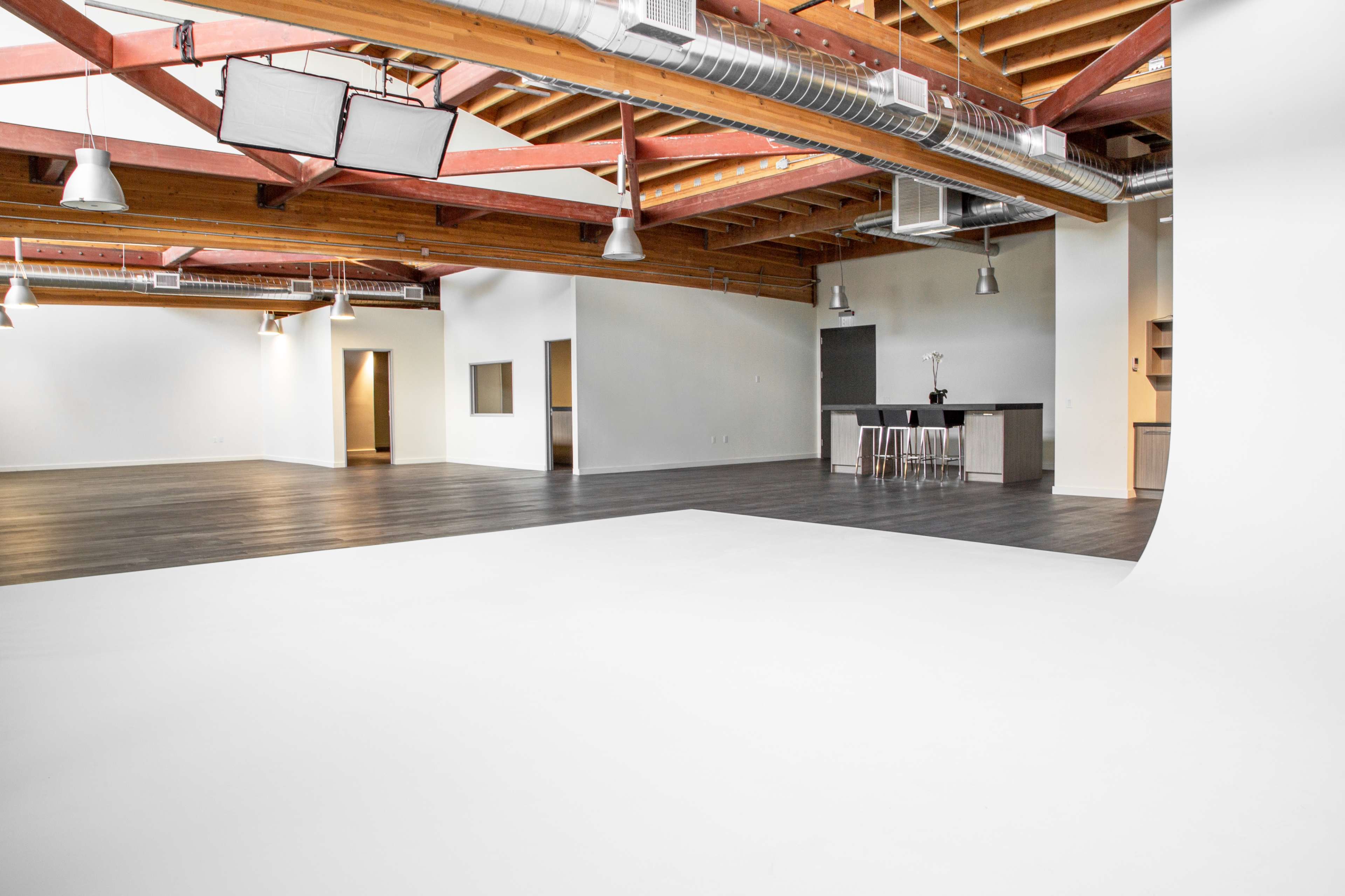 A spacious, well-lit studio with wooden beams and a white backdrop area, featuring a bar counter in the corner.