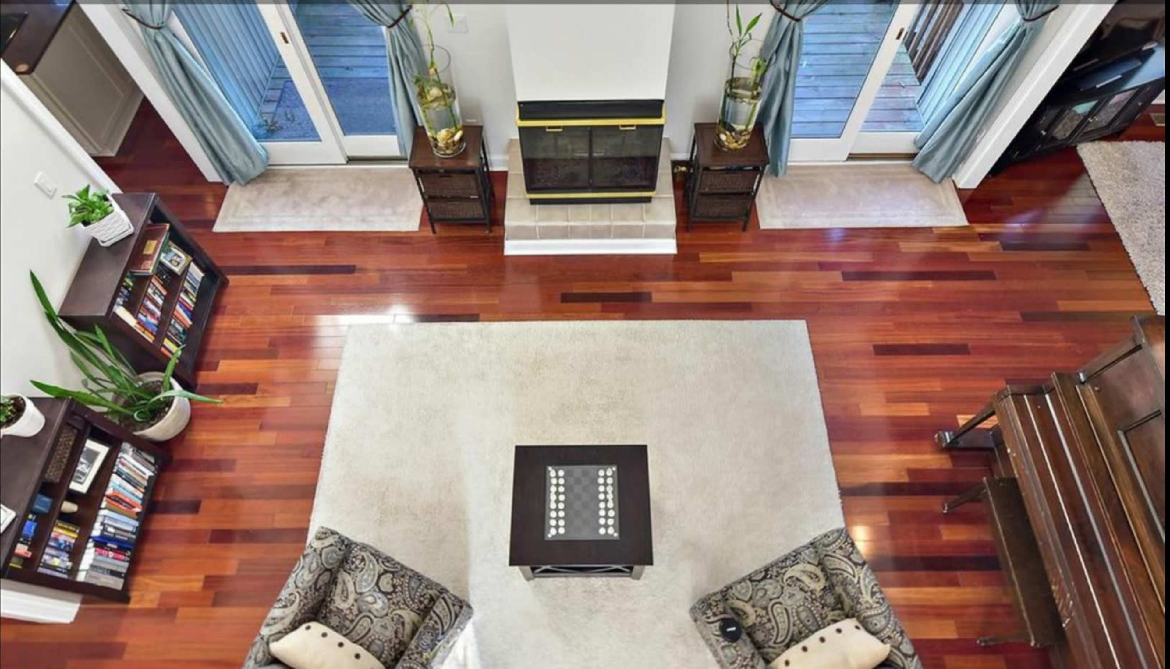 A spacious living room with hardwood floors, a central area rug, two patterned chairs, and a fireplace flanked by sliding glass doors.