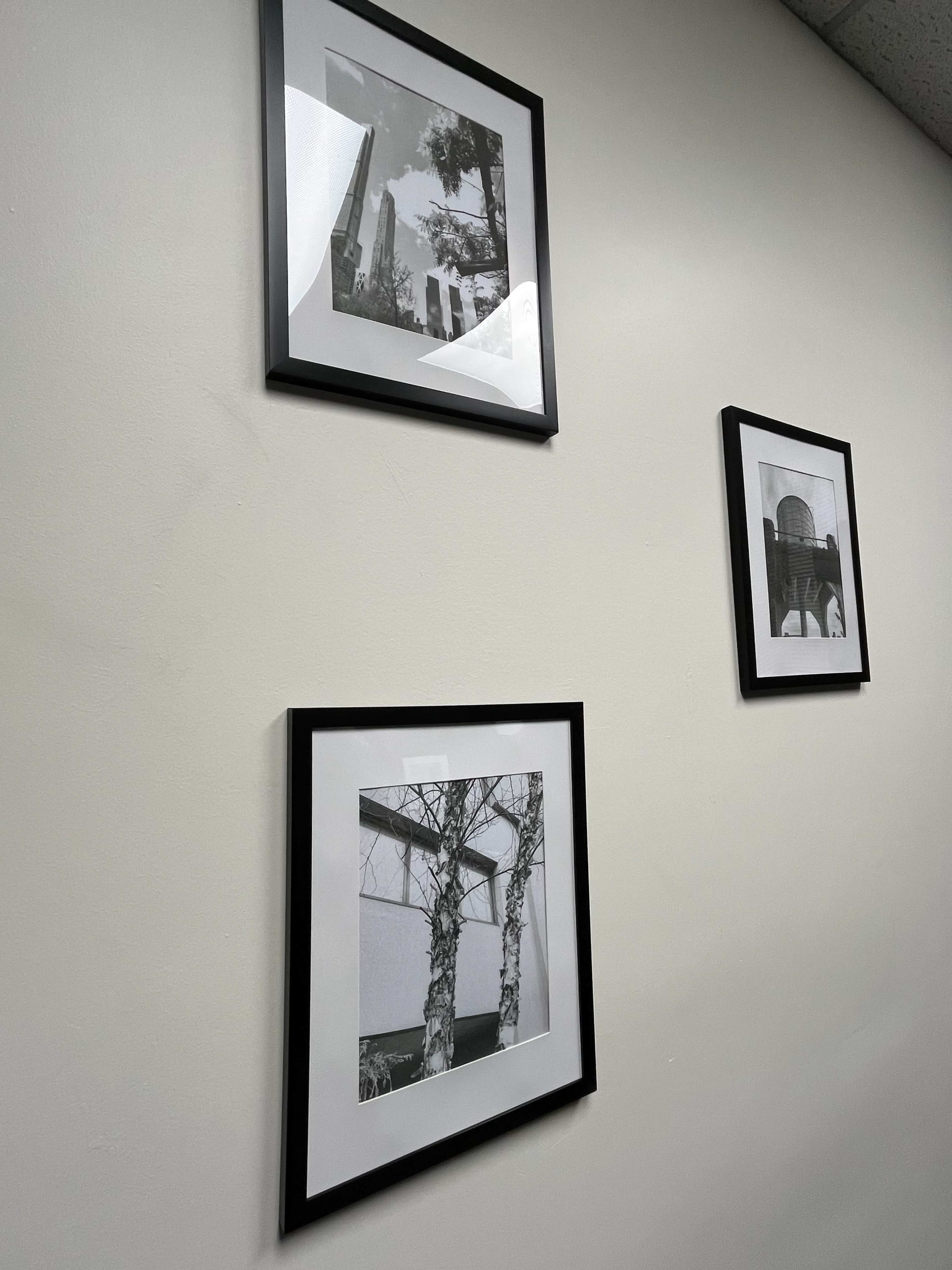 Three black and white photographs are framed and hung on a light-colored wall.