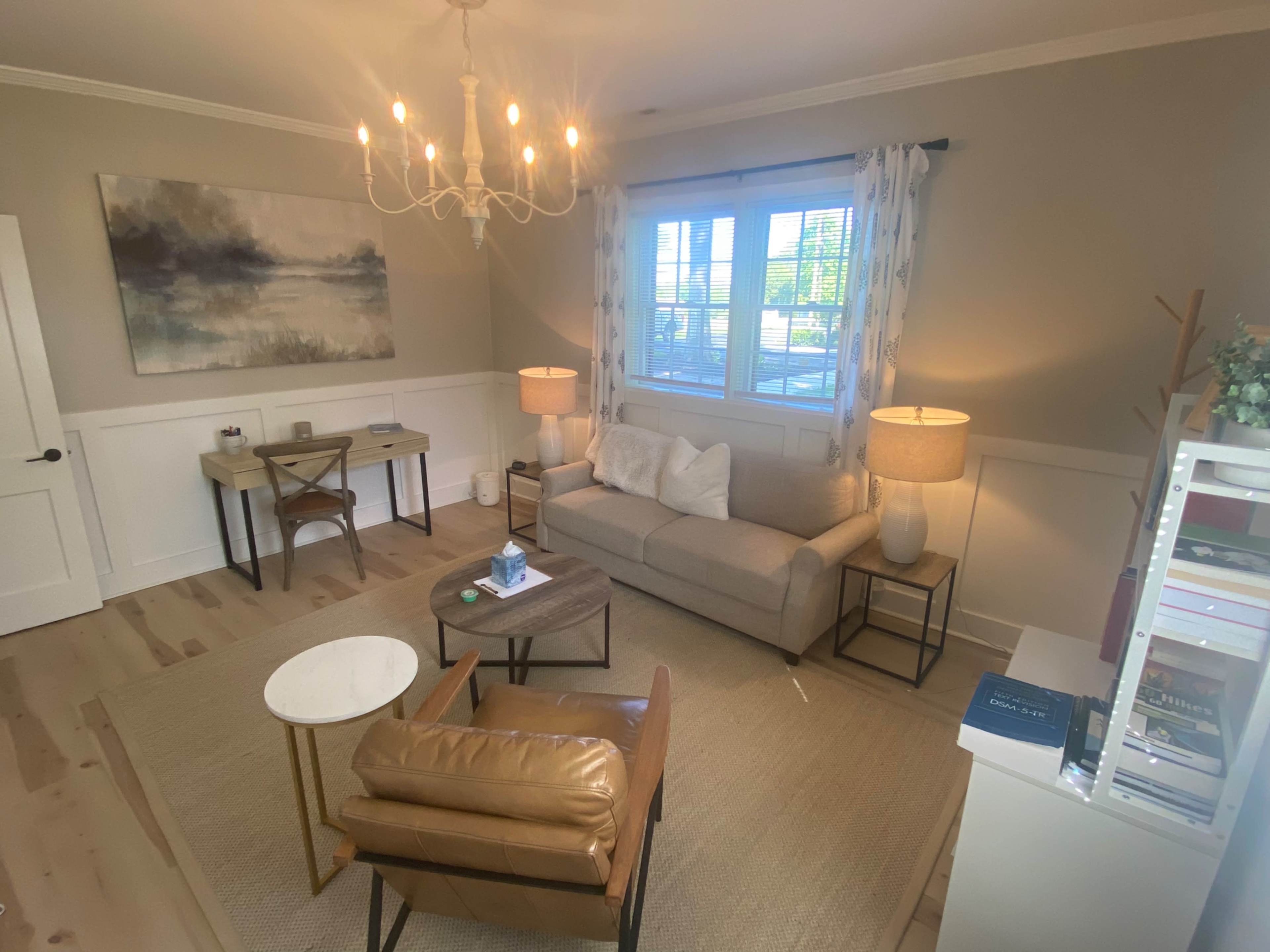 A cozy living room with a light-colored sofa, two lamps, a coffee table, and a workspace in the corner.