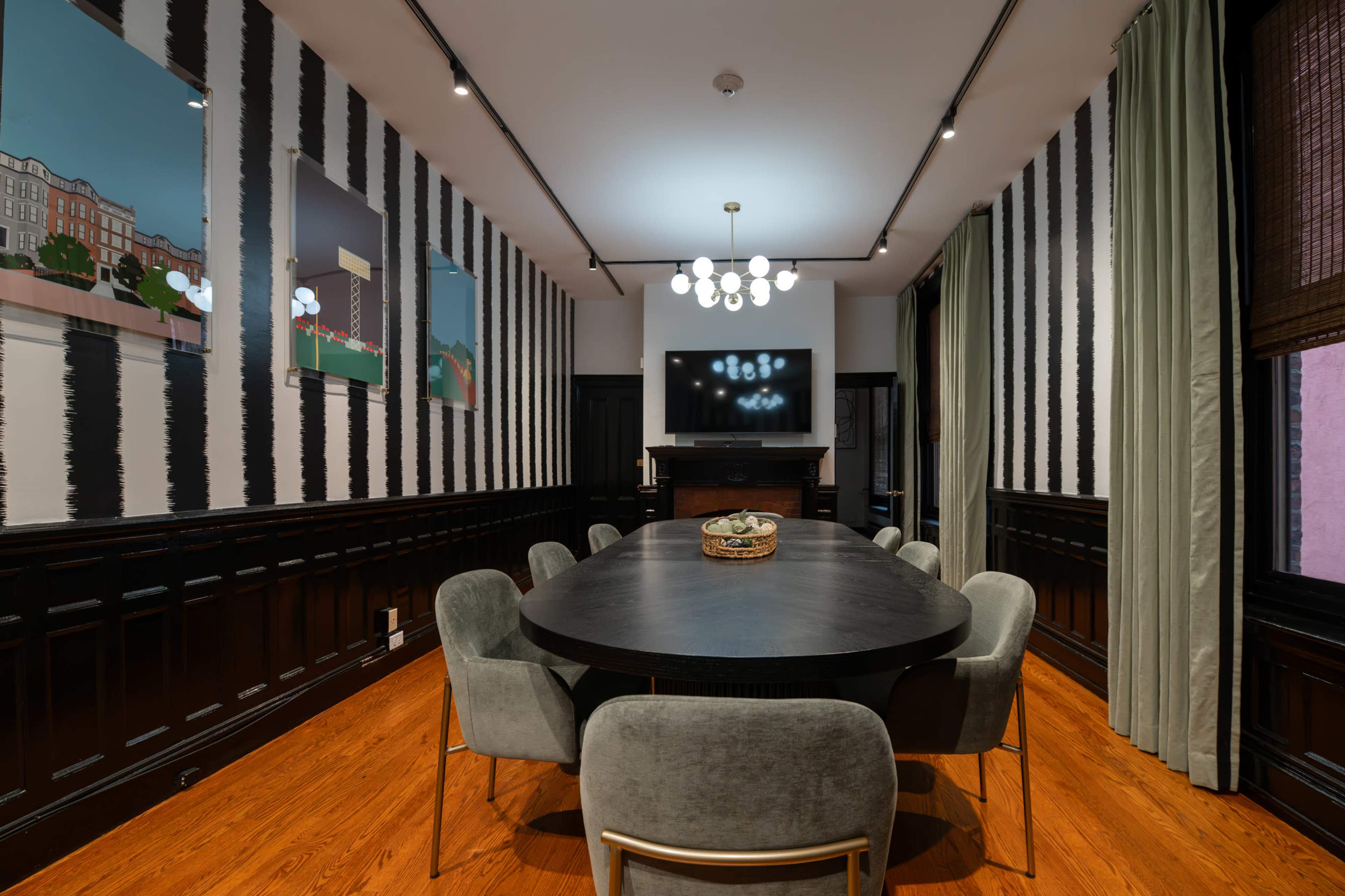 The image shows a dining room with a round black table surrounded by gray chairs, featuring striped wallpaper and framed artwork on the walls.
