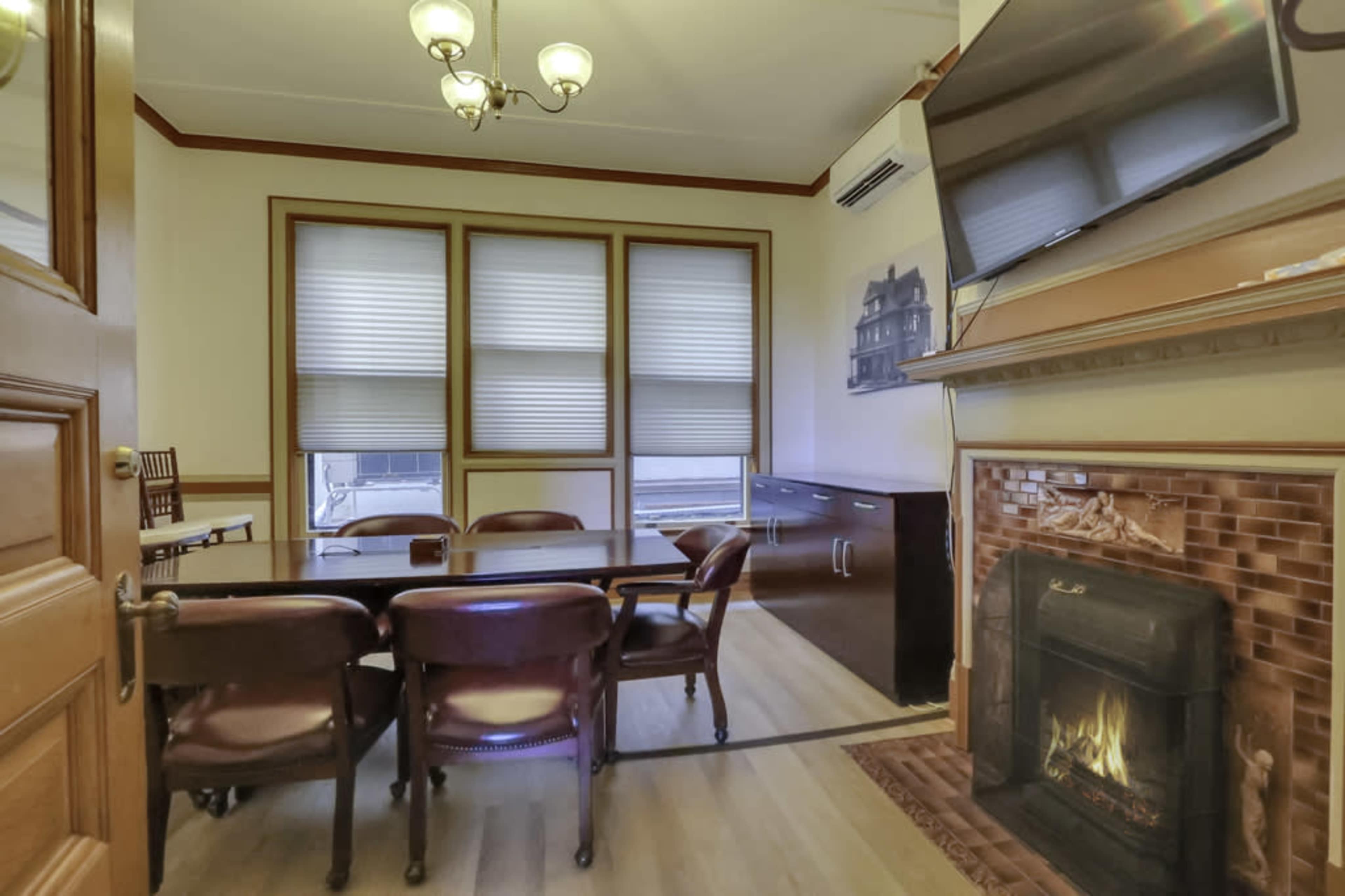 A conference room with a wooden table, several chairs, a wall-mounted television, and a fireplace.