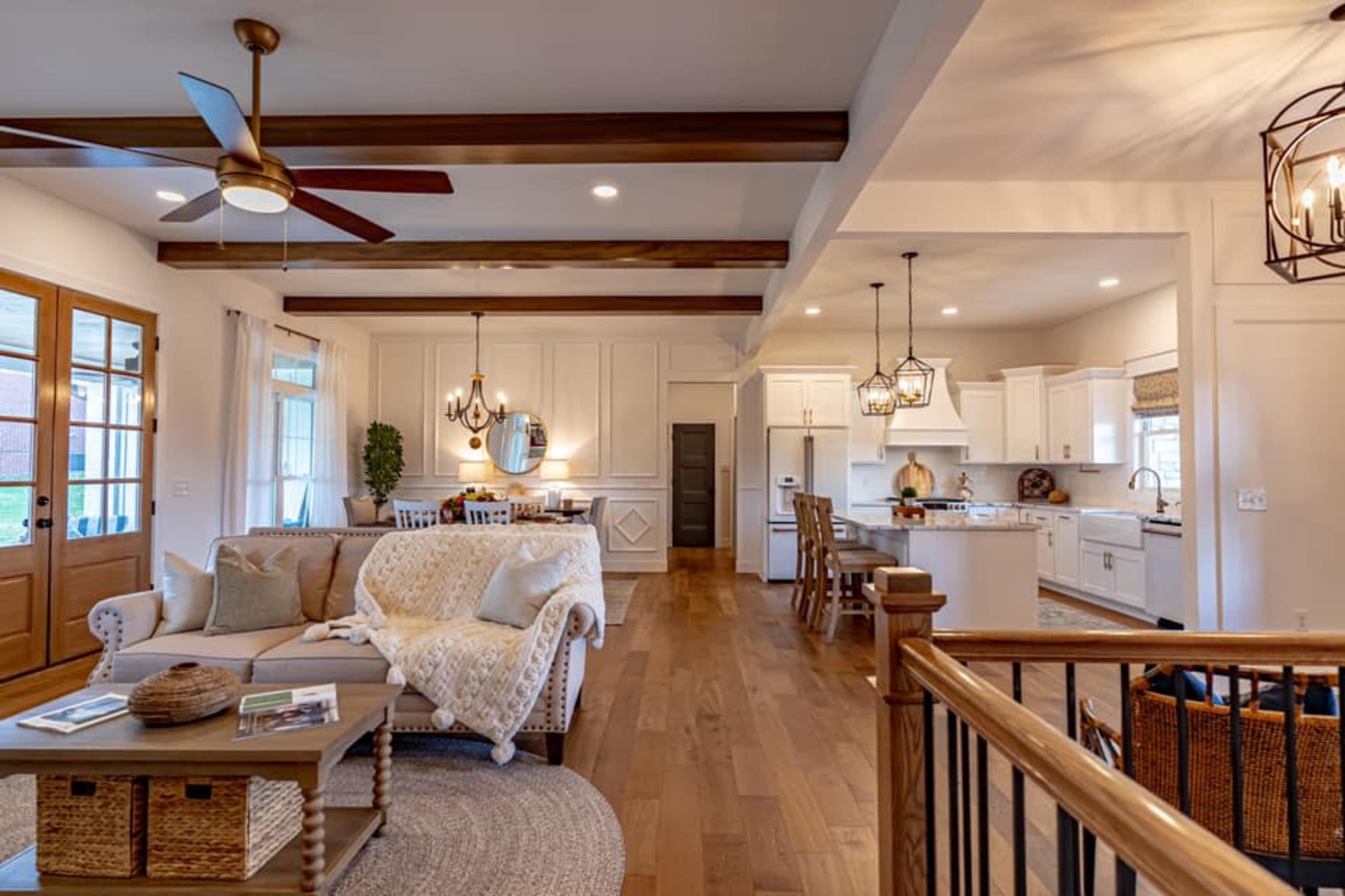 A spacious living area features a comfortable sofa, wooden beams, and a kitchen with white cabinetry visible in the background.
