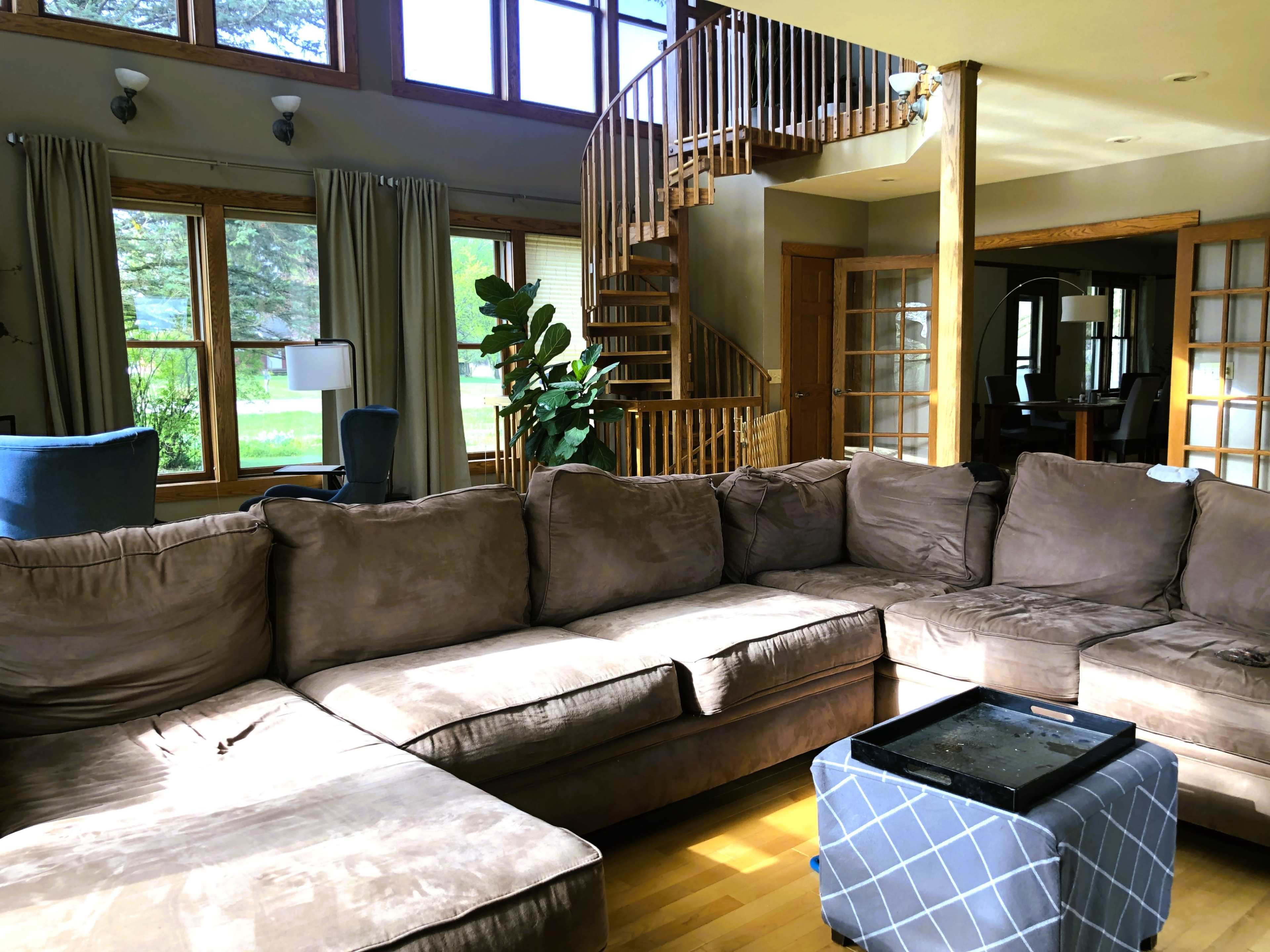 A spacious living room with a large sectional sofa, a glass coffee table, and a spiral staircase leading to an upper level, illuminated by natural light from large windows.