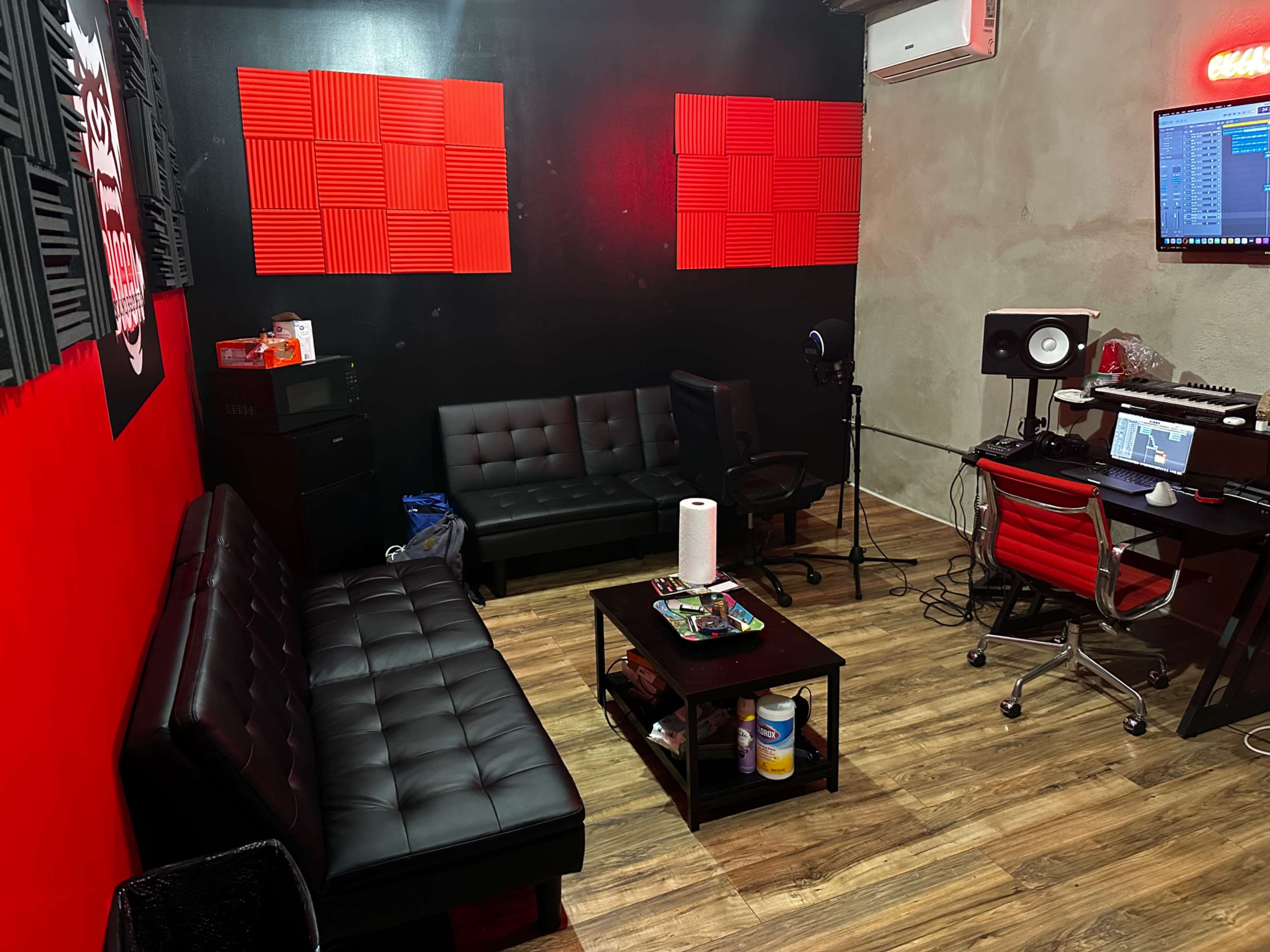 A small recording studio with soundproofing panels on the walls, a desk with audio equipment, a black sofa, and a coffee table.