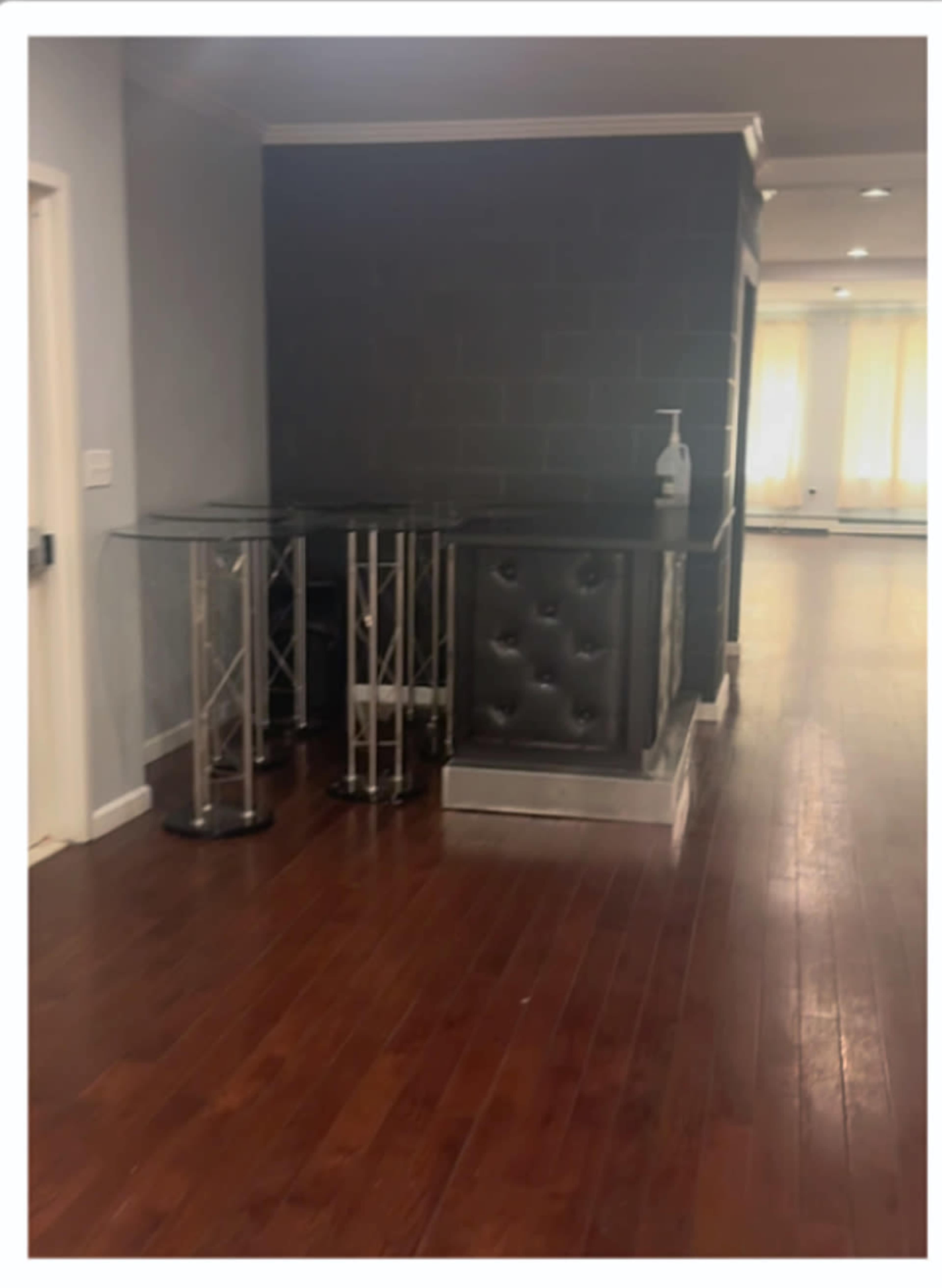 A small corner area features two clear glass tables and a dark, tufted counter against a gray wall with wooden flooring.