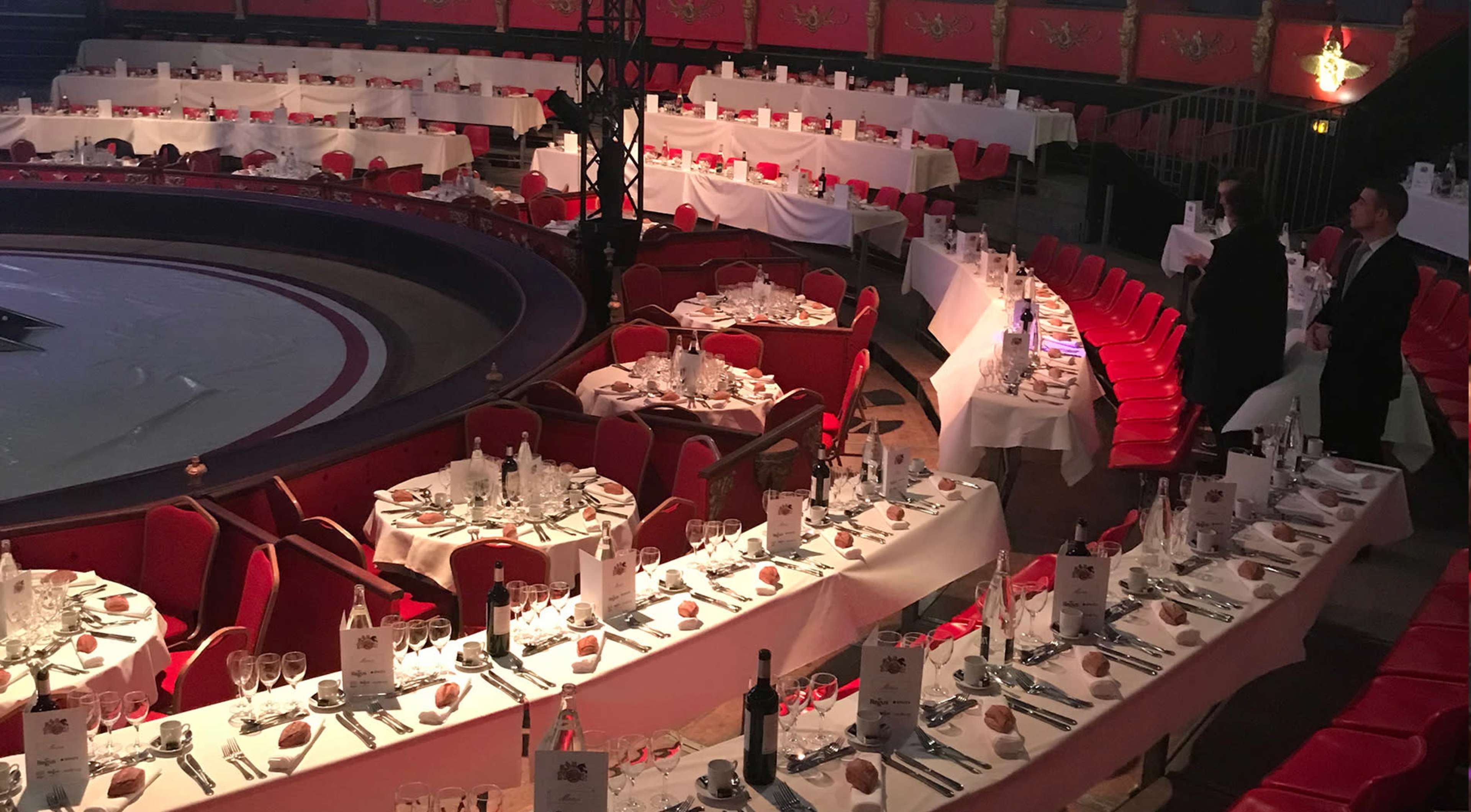 A circular banquet hall set with numerous elegantly arranged dining tables surrounded by red chairs.