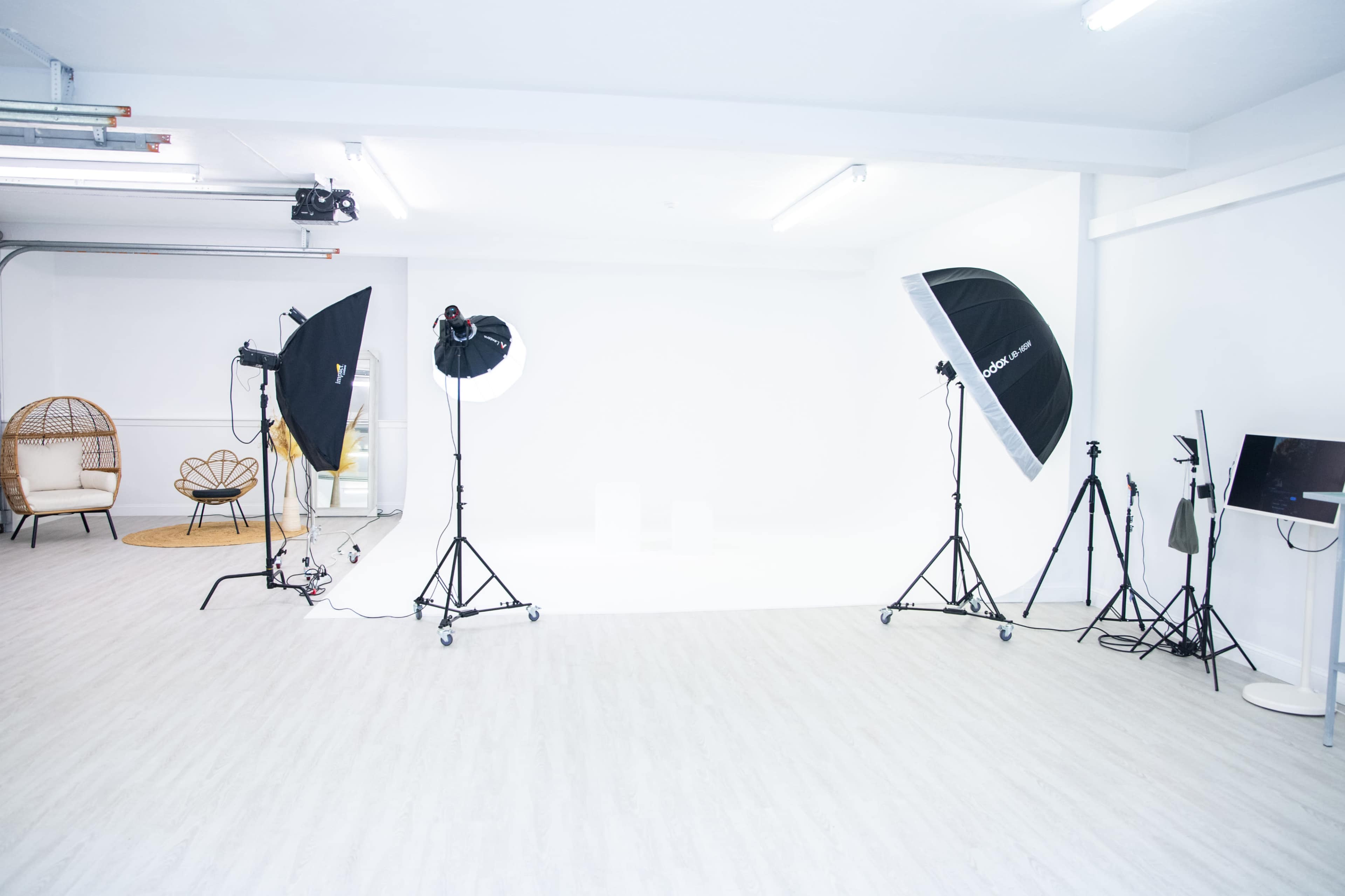 A photography studio is set up with lighting equipment, backdrops, and seating arranged in a well-lit, white space.