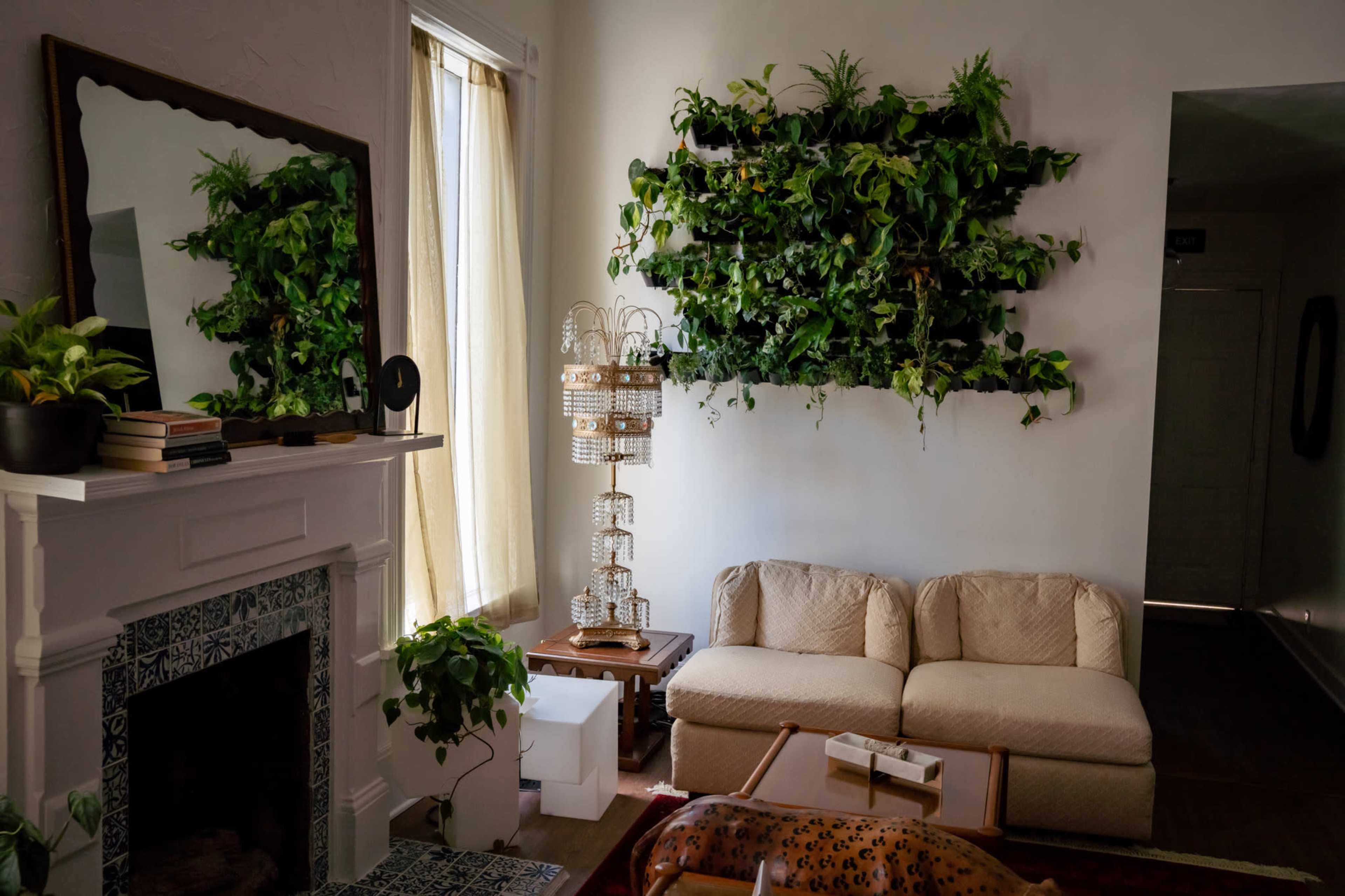 A living room features a beige sofa, a wall of vertical greenery, a decorative mirror, and a small table with books.