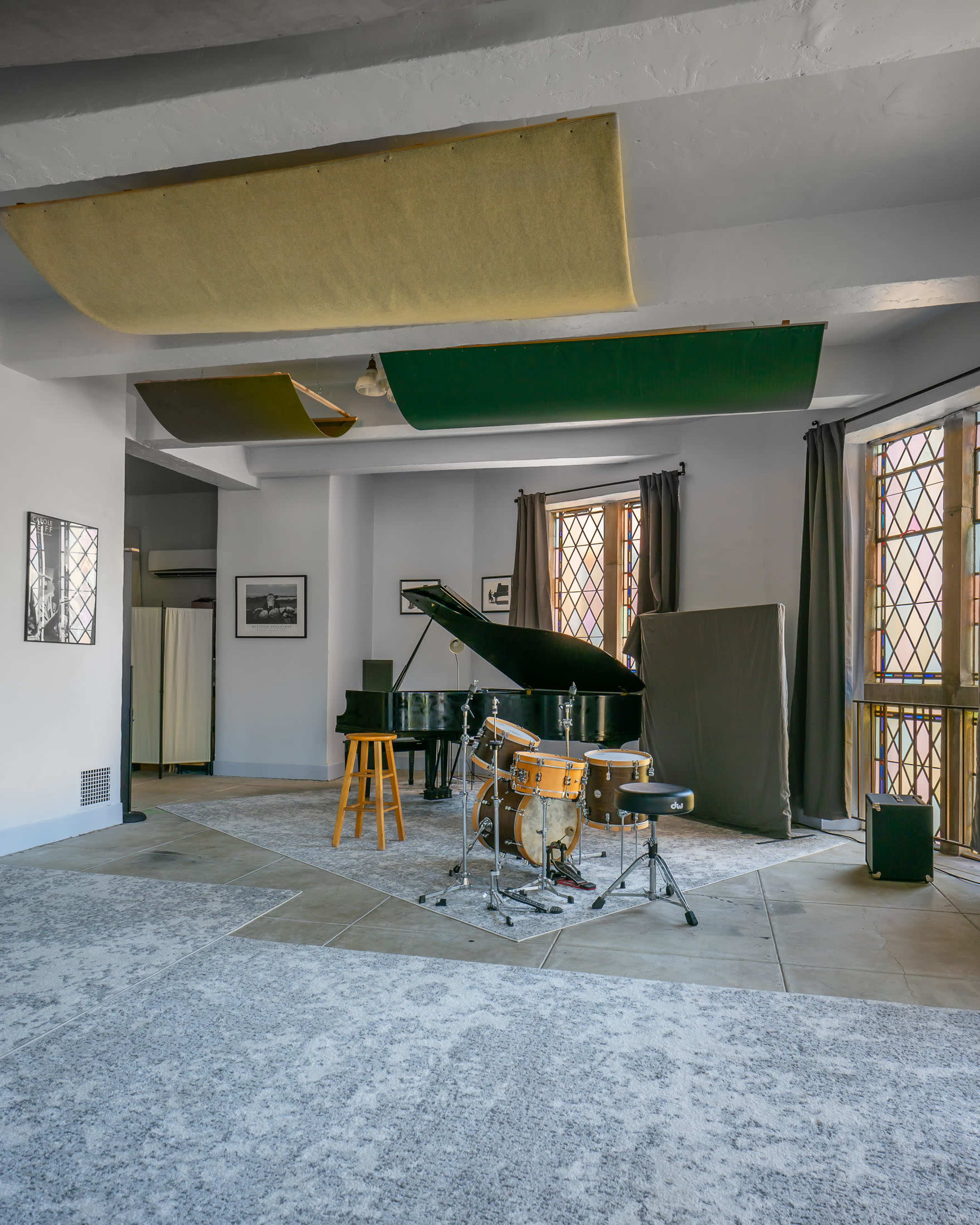 The image features a music studio with a grand piano, a drum set on a raised platform, and acoustic panels hanging from the ceiling.