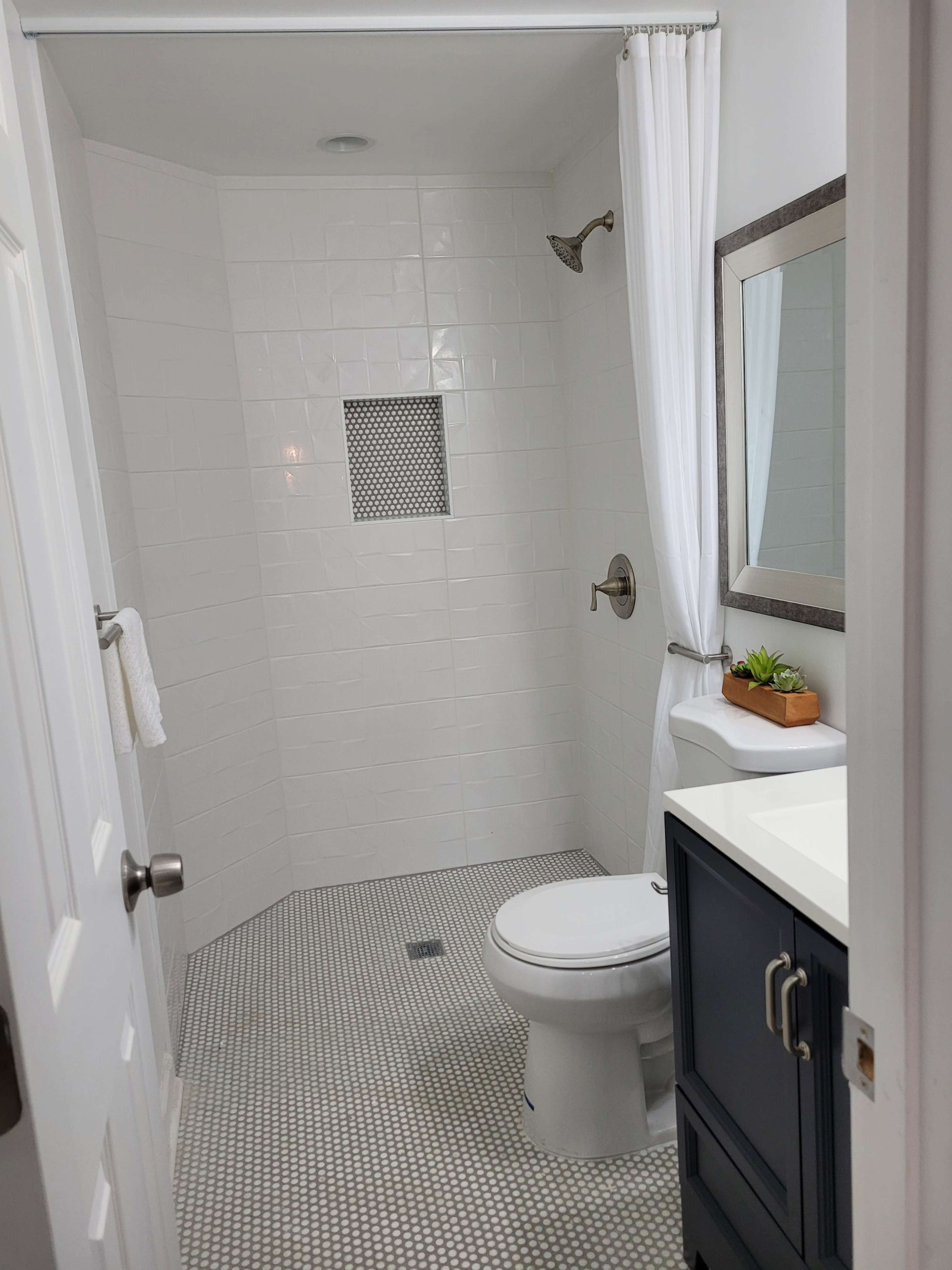 A modern bathroom featuring a shower with a tiled wall, a toilet, and a sink with a mirror, all surrounded by white walls and a patterned floor.