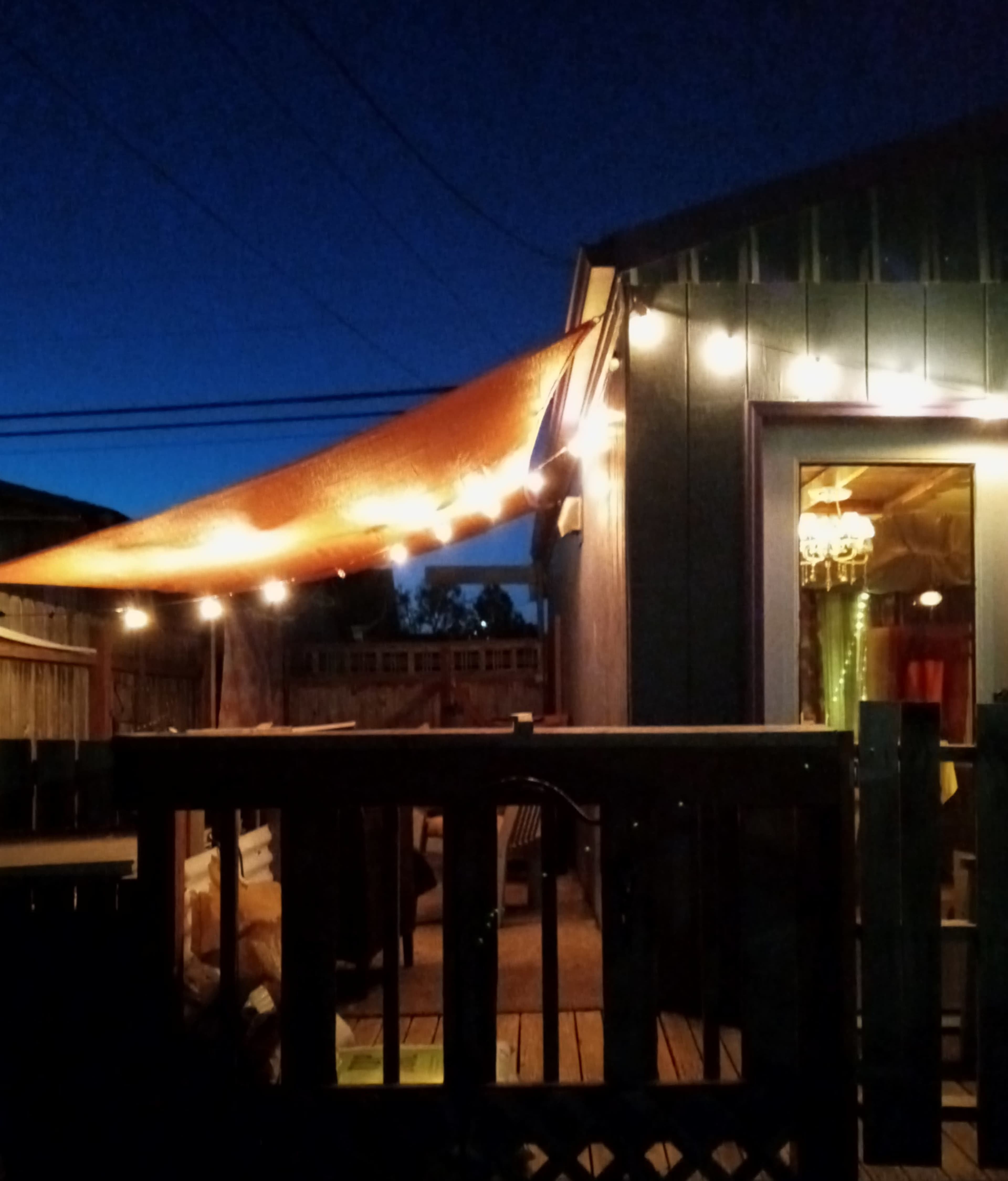 A patio is illuminated by string lights and a fabric canopy under a twilight sky.