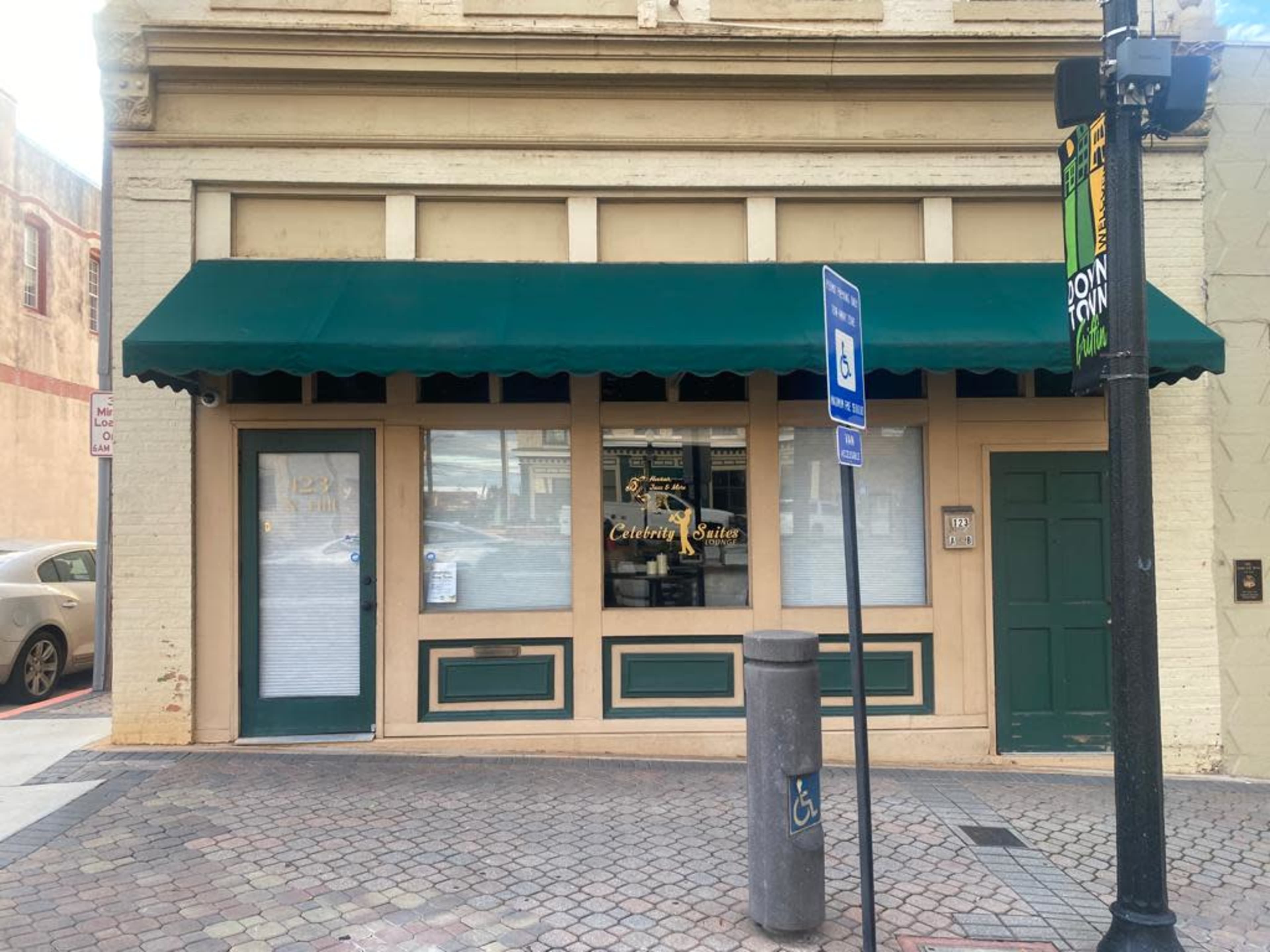 A storefront with a green awning and large windows, located at the corner of a street.
