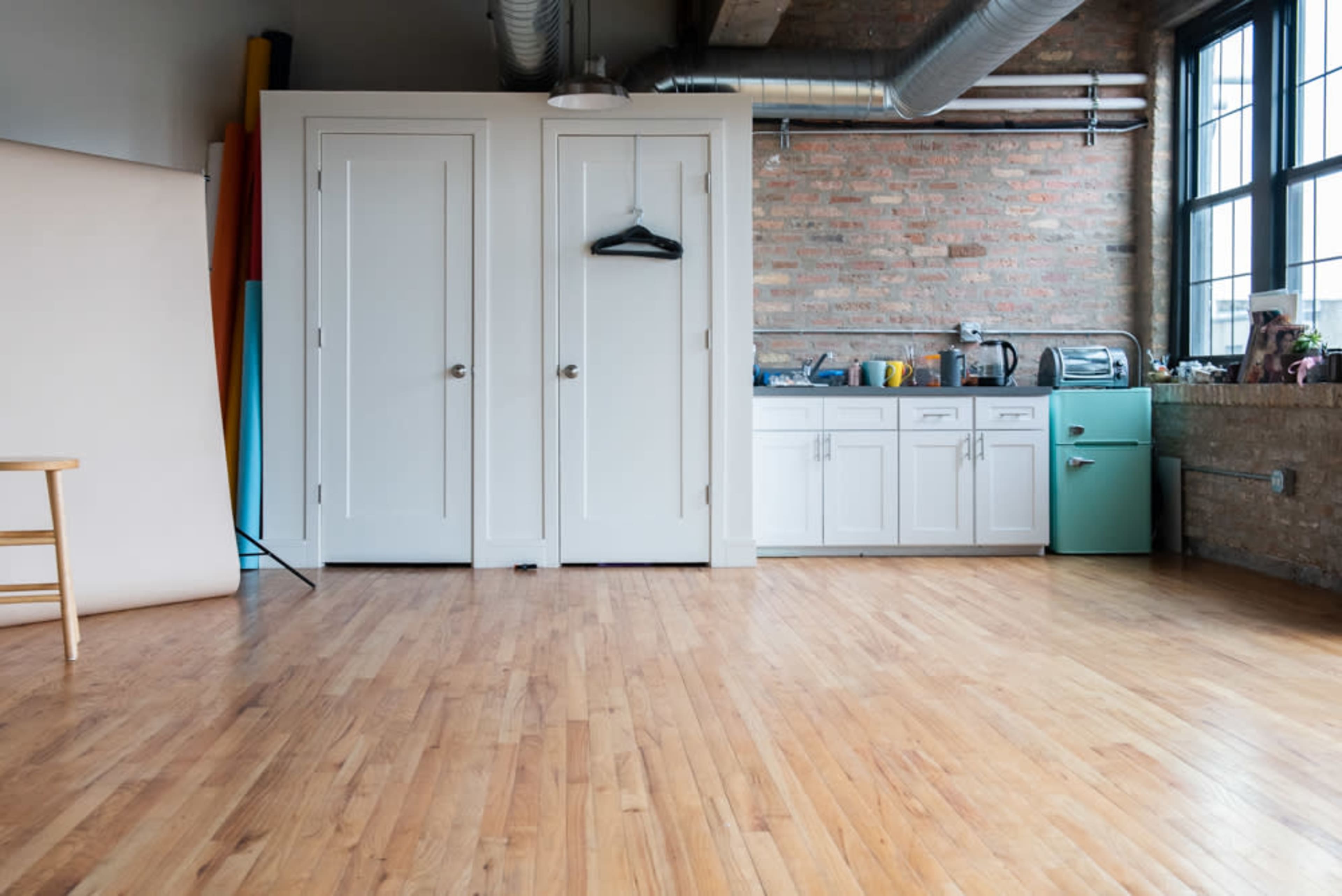 A spacious room with wooden flooring, a kitchenette featuring a mint green appliance, and two white closet doors.