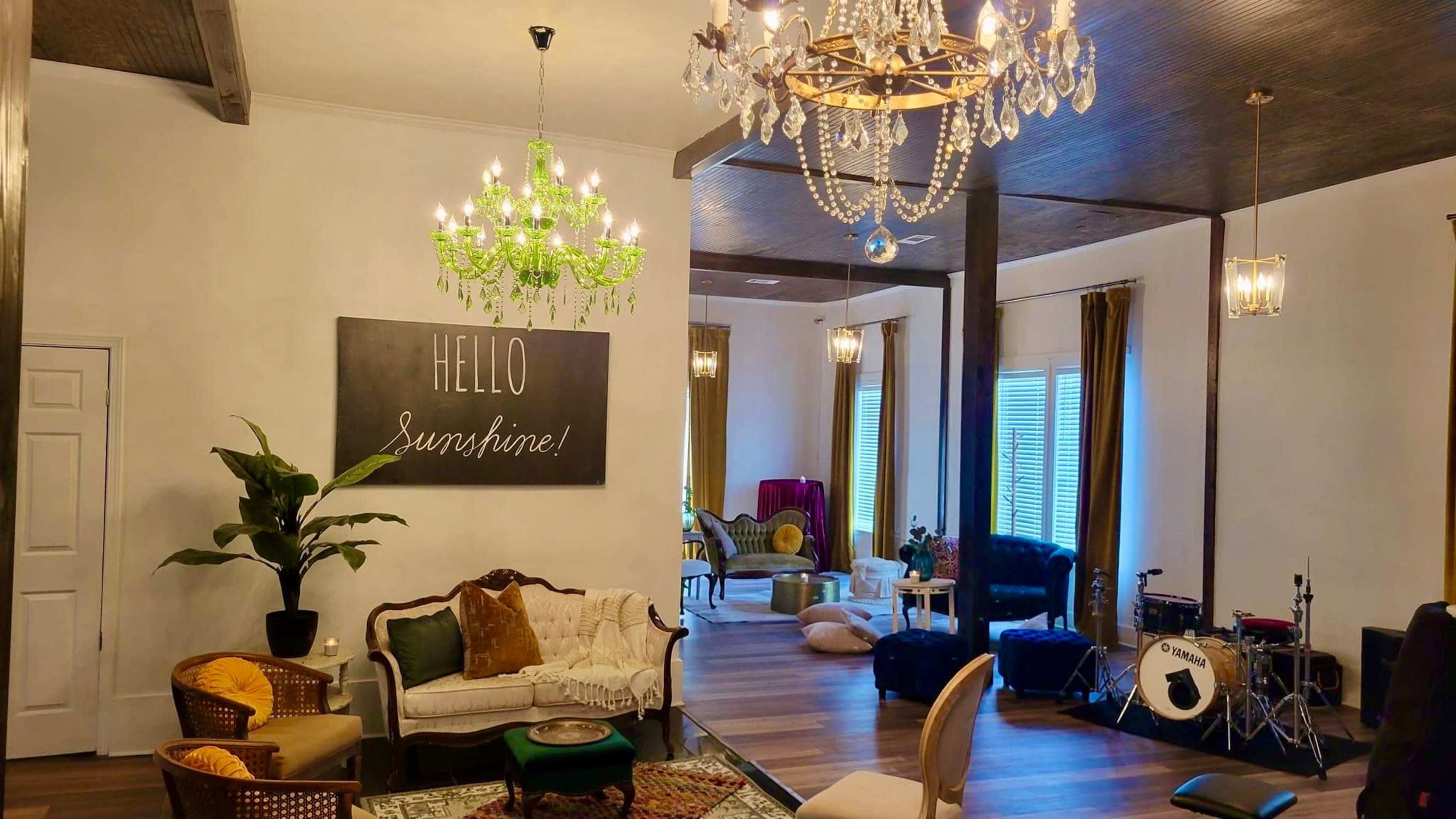 The image shows a brightly lit, spacious room featuring vintage furniture, decorative chandeliers, and a large blackboard with the words "HELLO Sunshine!" written on it.