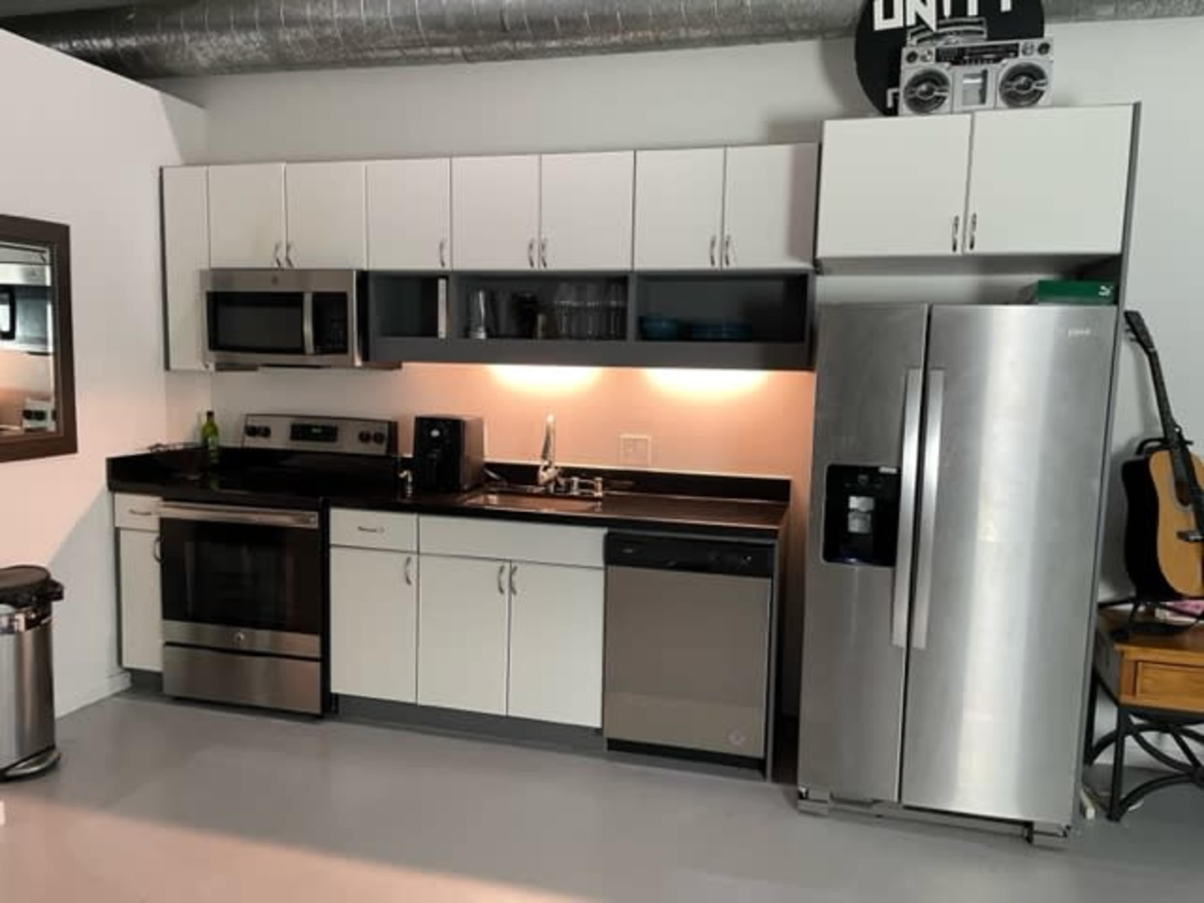 The image shows a modern kitchen equipped with stainless steel appliances, white cabinets, and a black countertop.
