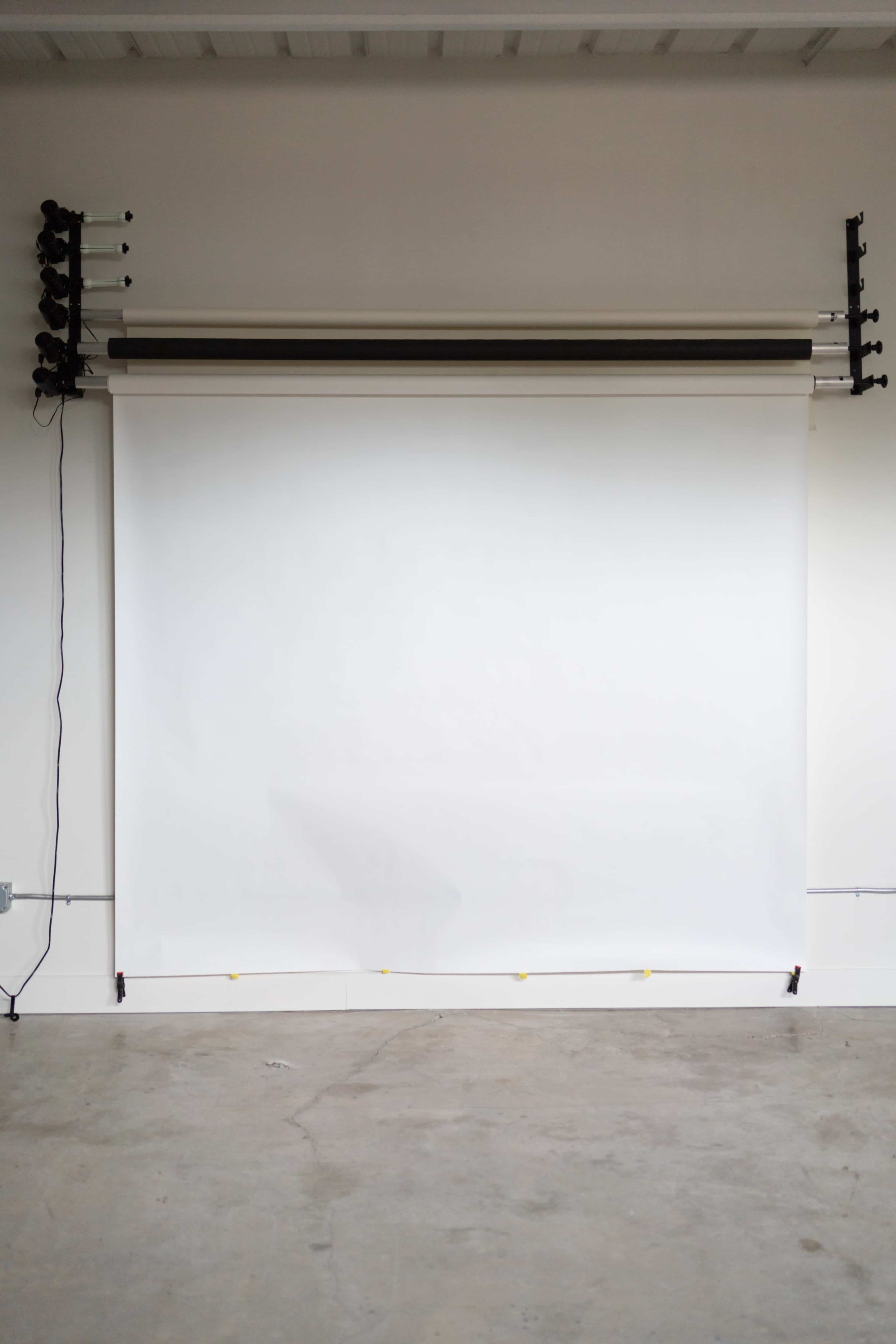 The image shows a blank white backdrop set up in a minimalist studio environment.