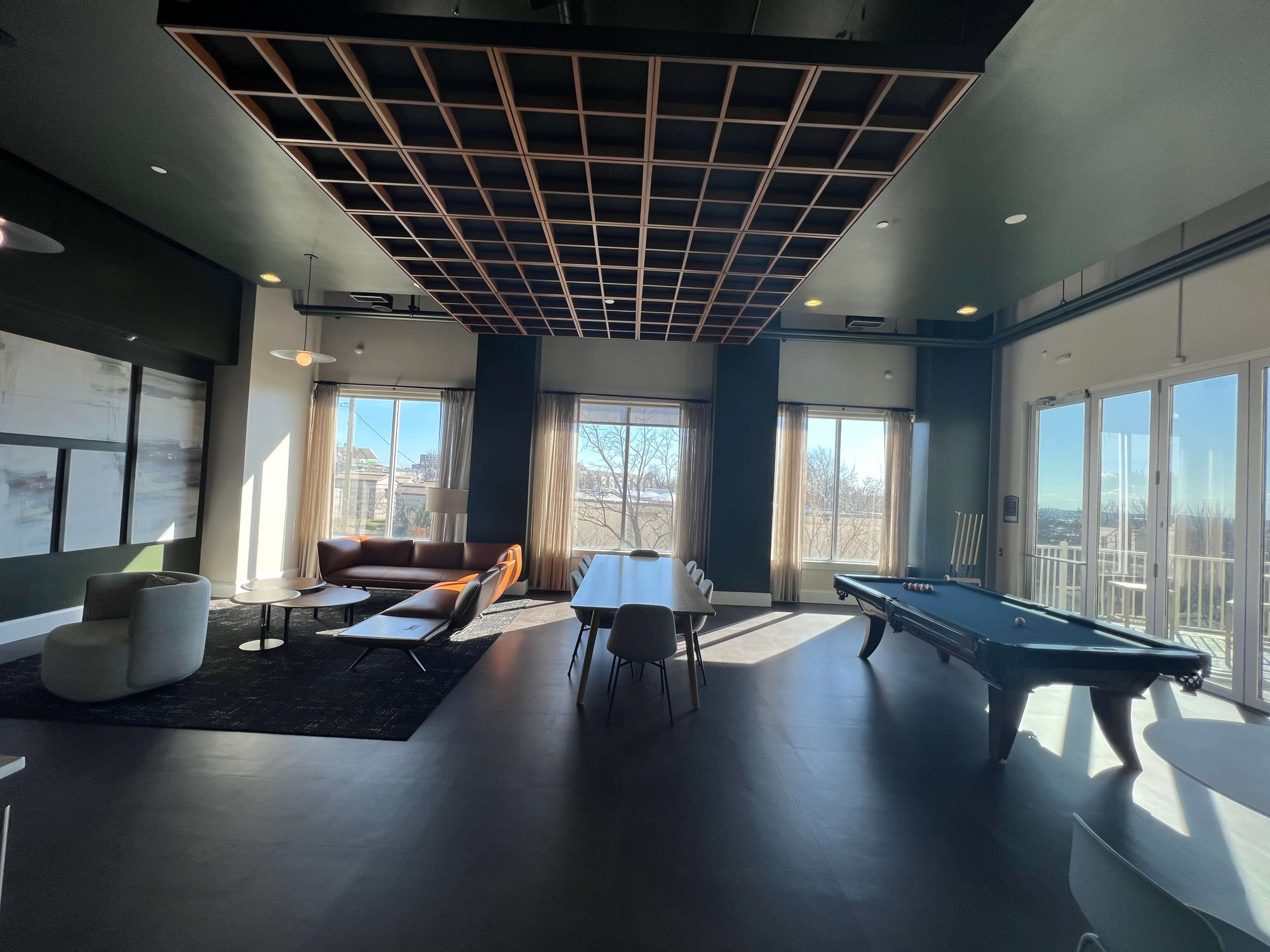 A modern room with a pool table, a dining area, a lounge seating arrangement, and large windows that provide a view of an outdoor landscape.