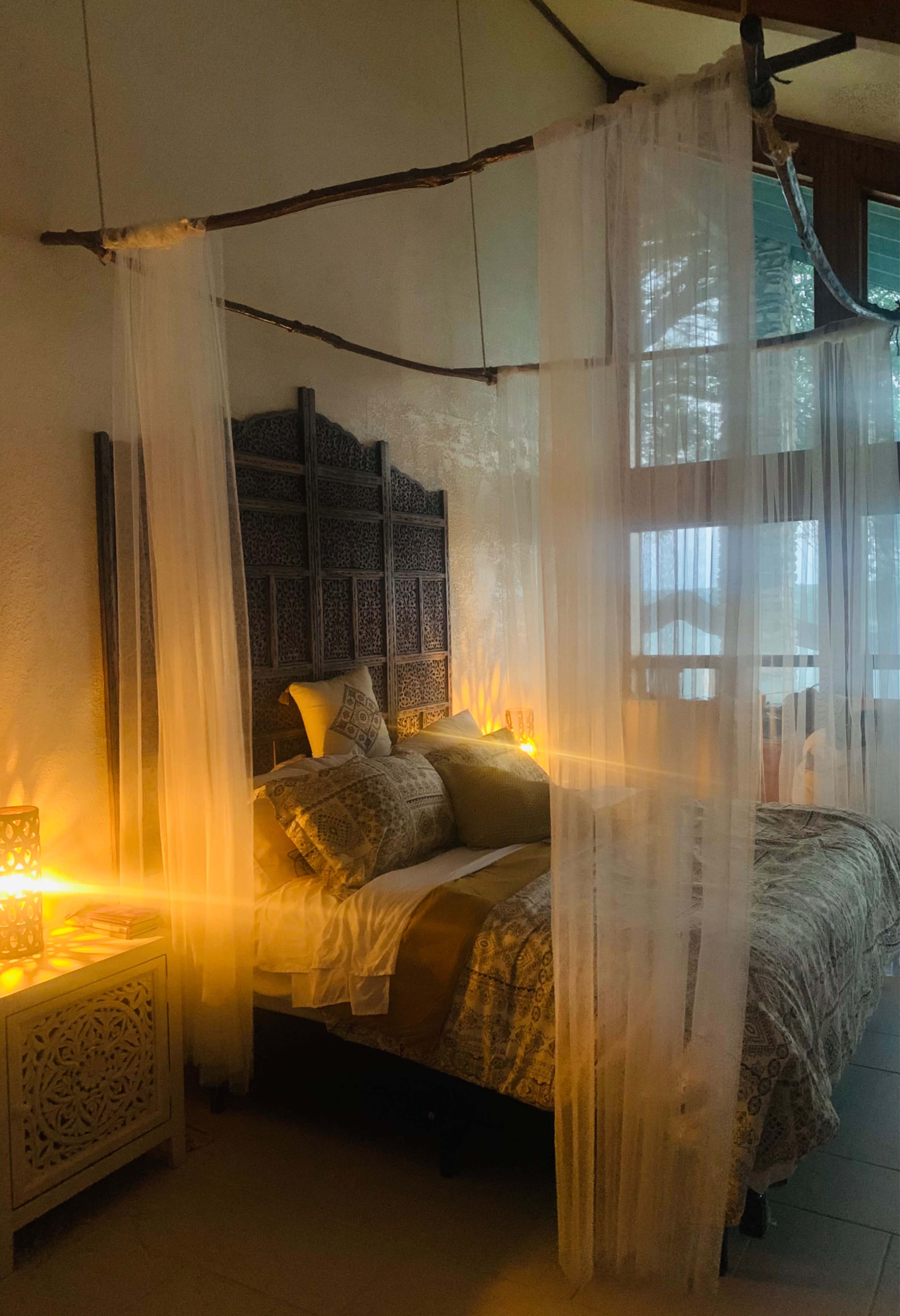 A bed with a patterned quilt is framed by sheer curtains and complemented by decorative lanterns in a softly lit room.
