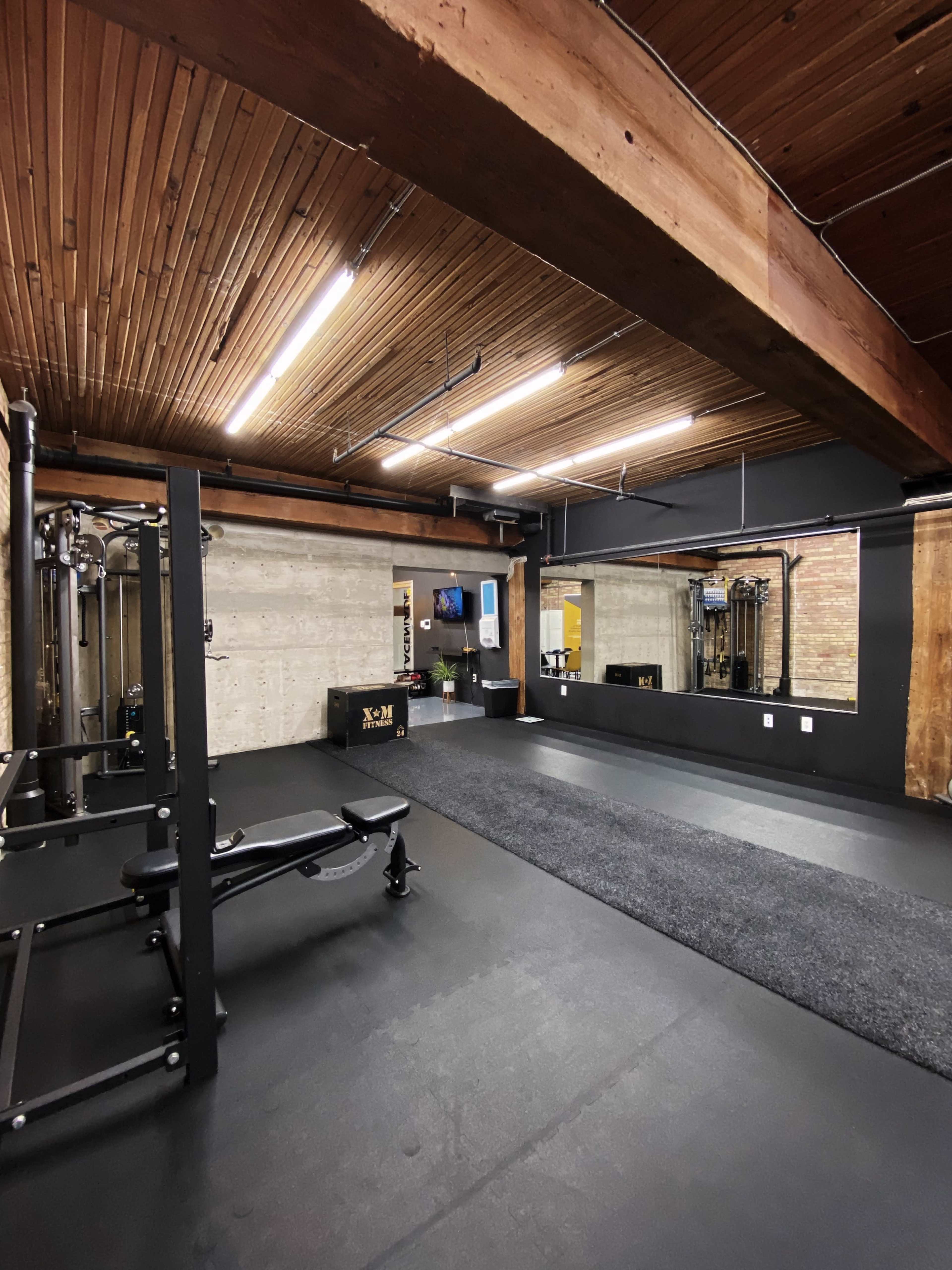 A modern home gym featuring black flooring, wooden ceilings, exercise equipment, and a large mirror.