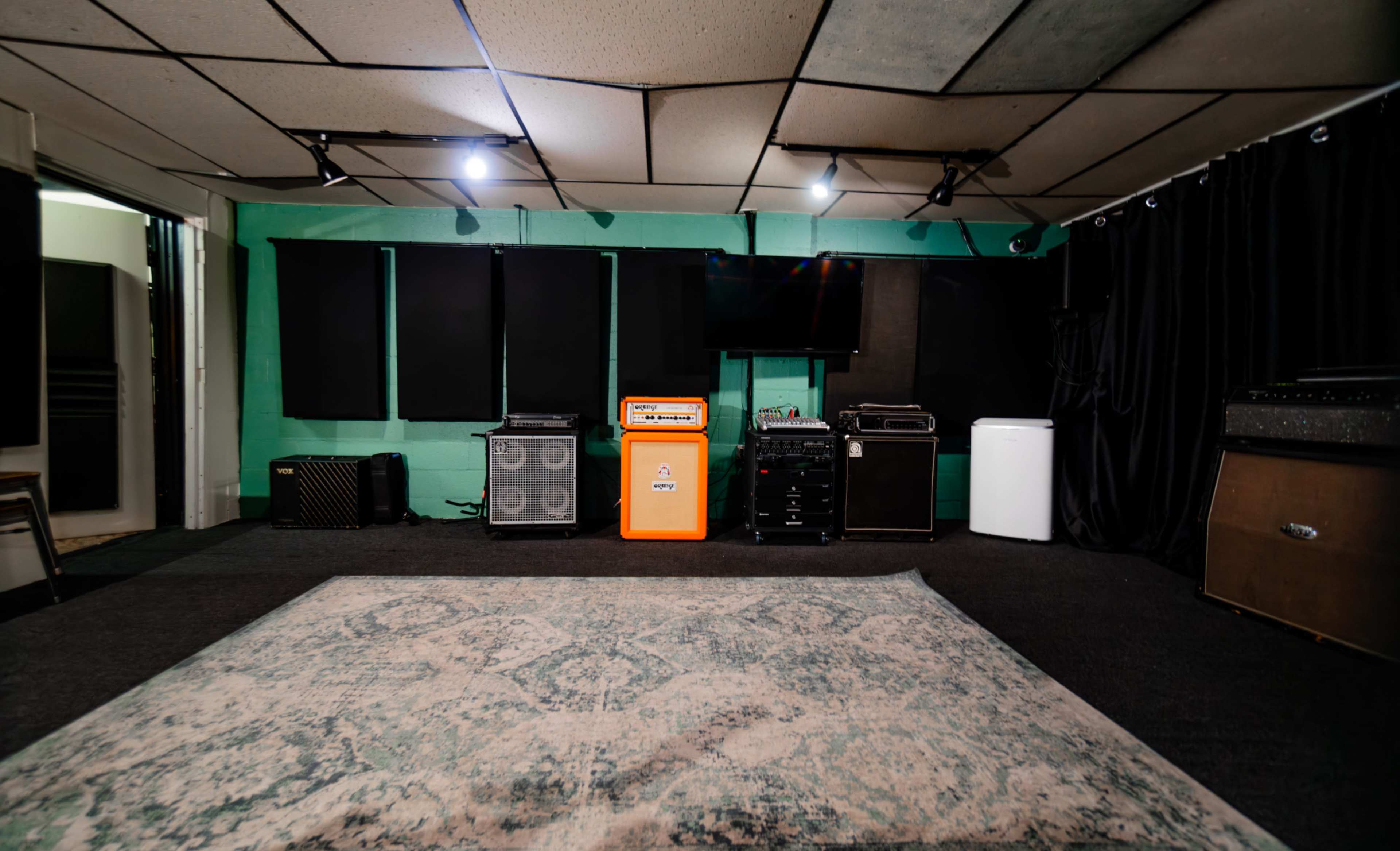 A music studio with various amplifiers, a television, and a patterned rug on the floor.