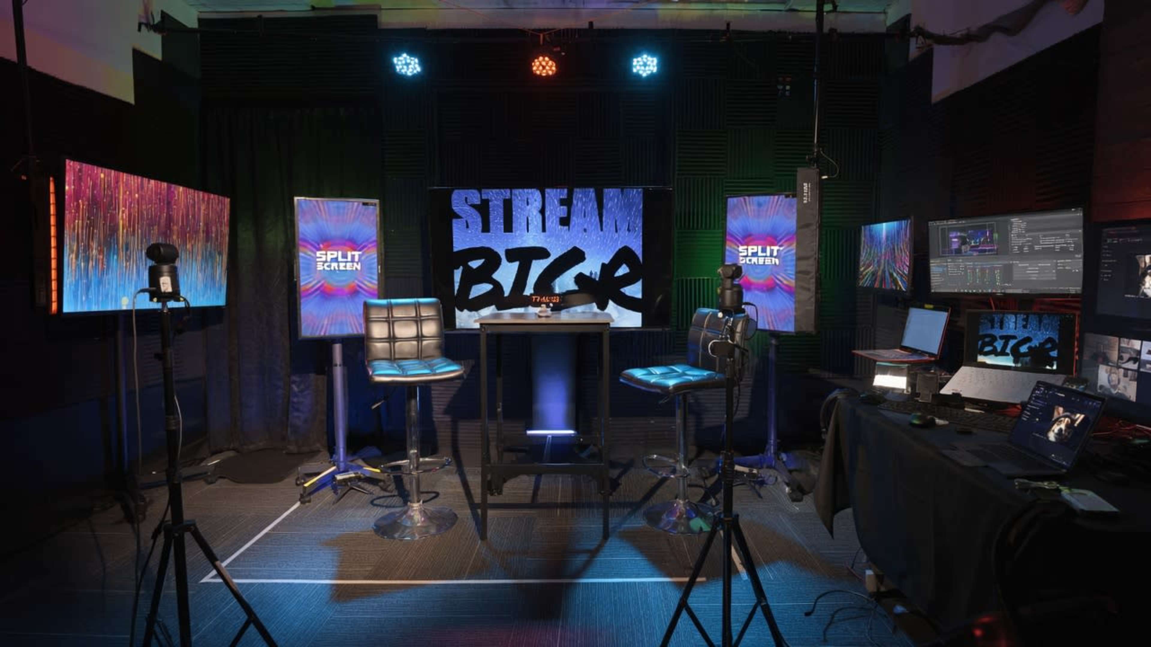 The image shows a professional streaming studio setup with two high stools, multiple screens displaying vibrant graphics, and various camera and lighting equipment.