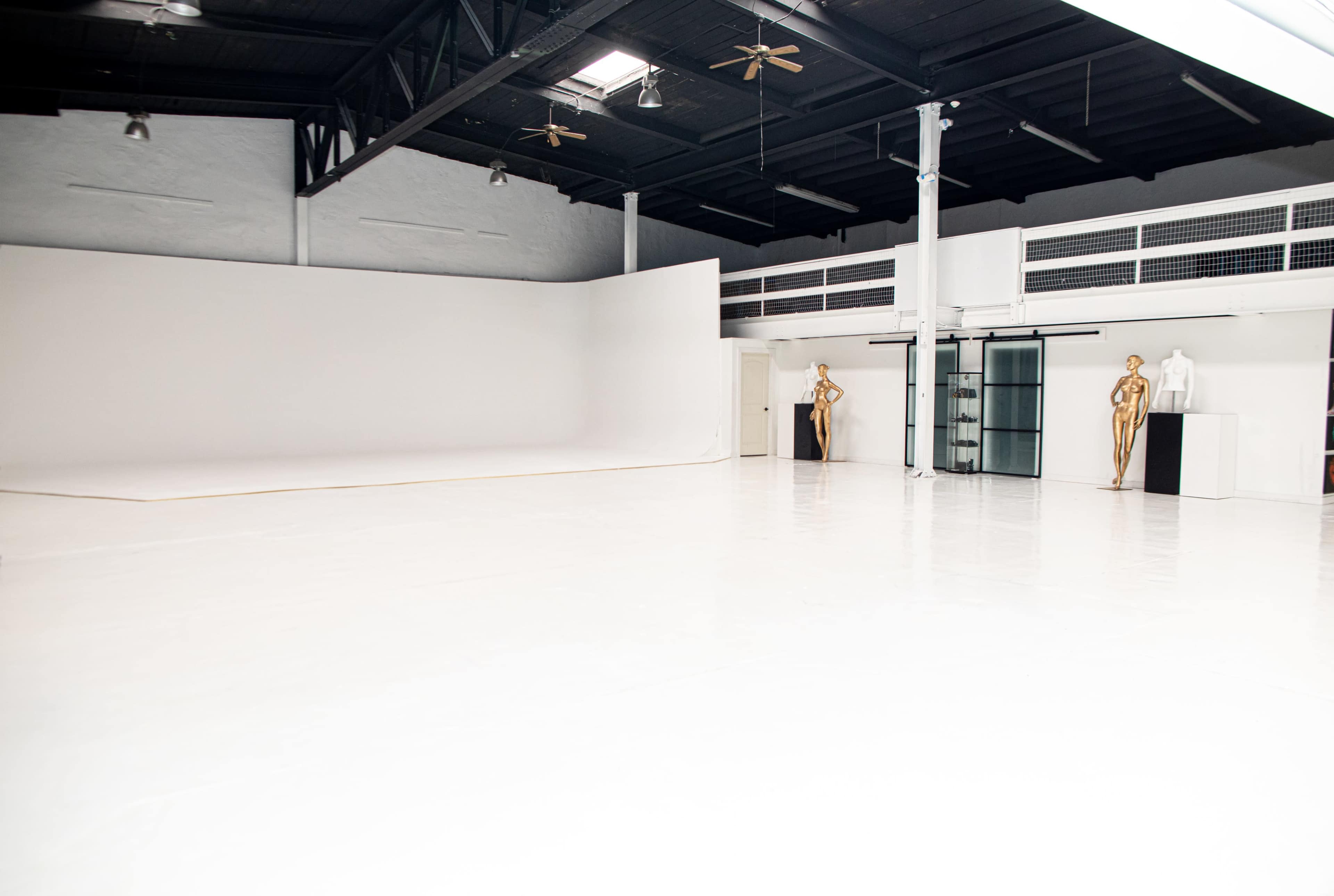 The image shows a spacious studio with white walls, a polished floor, and several mannequins positioned along one side.